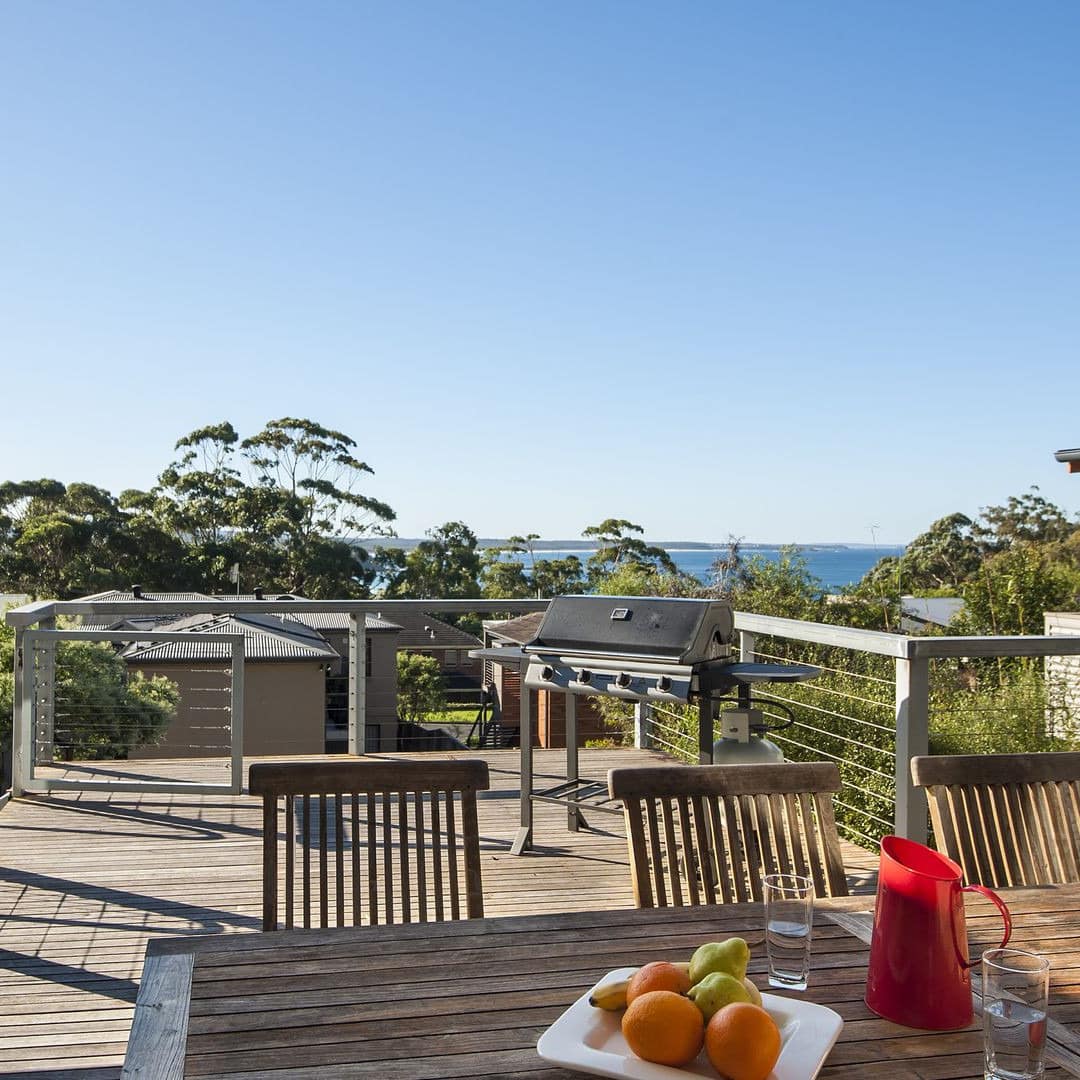 Deck of beach house with table and chairs with distant view of the beach which is a short walk away