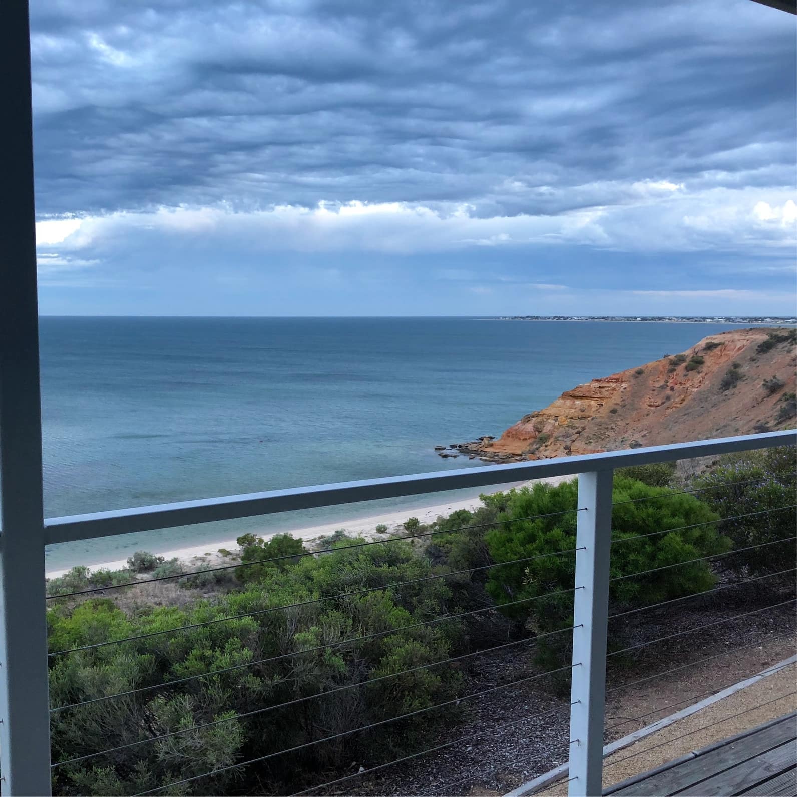 View overlooking a sandy beach, cliffs and lush vegetation from a balcony with metal railings.
