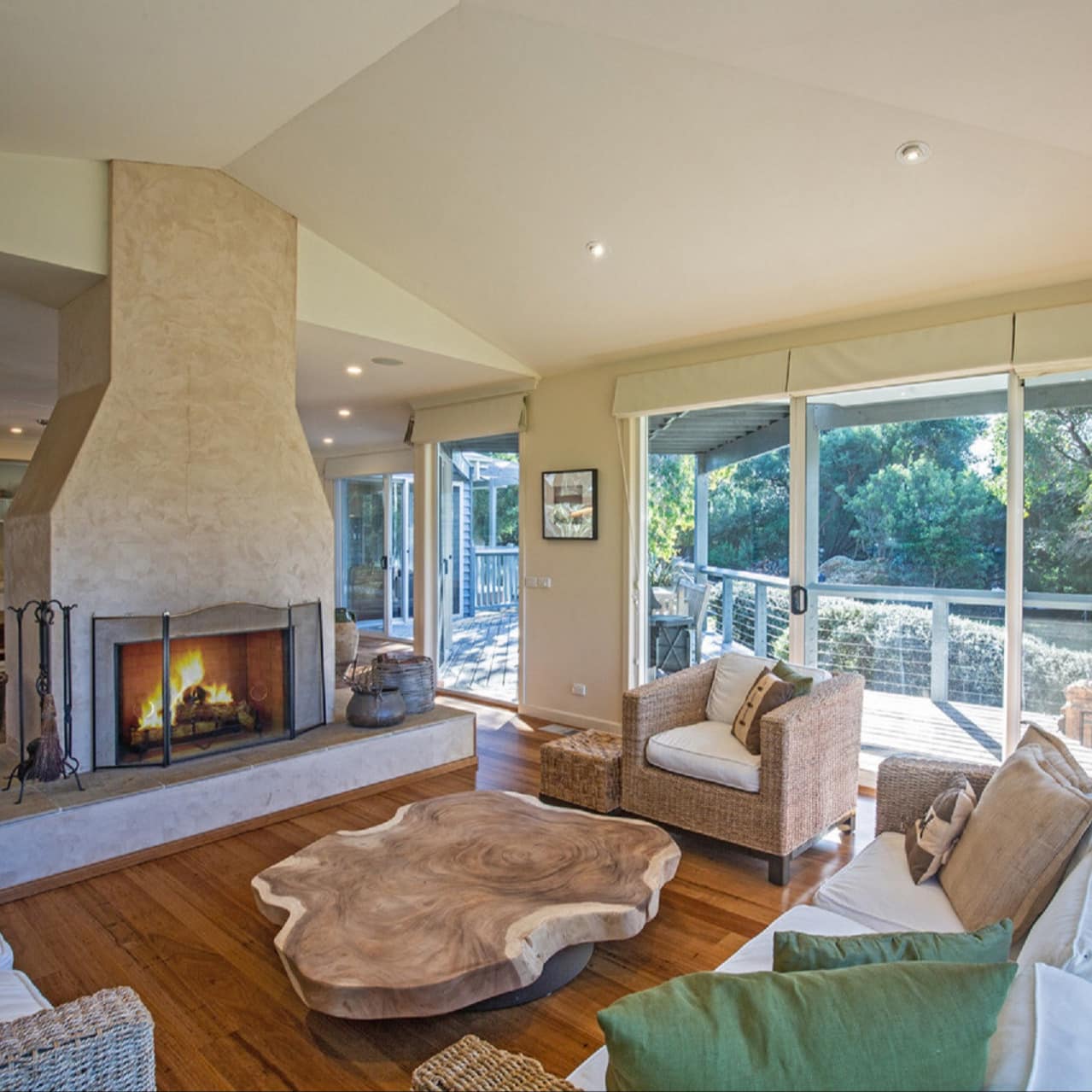 Open living room with hardwood floors, a fireplace, matching wicker sofa and chairs, natural wood coffee table, tall windows.