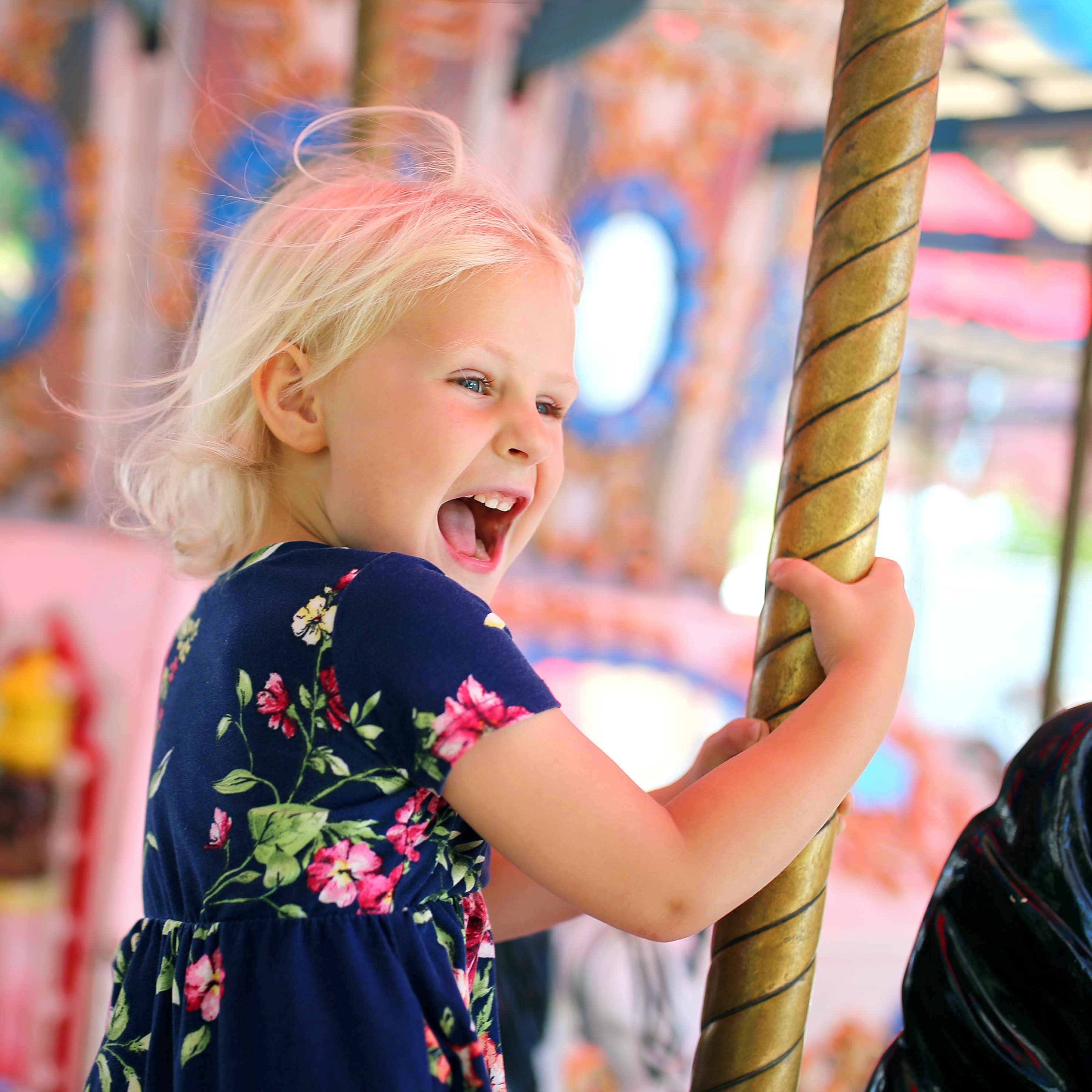 Happy young girl with mouth open riding on carousel with blurred background