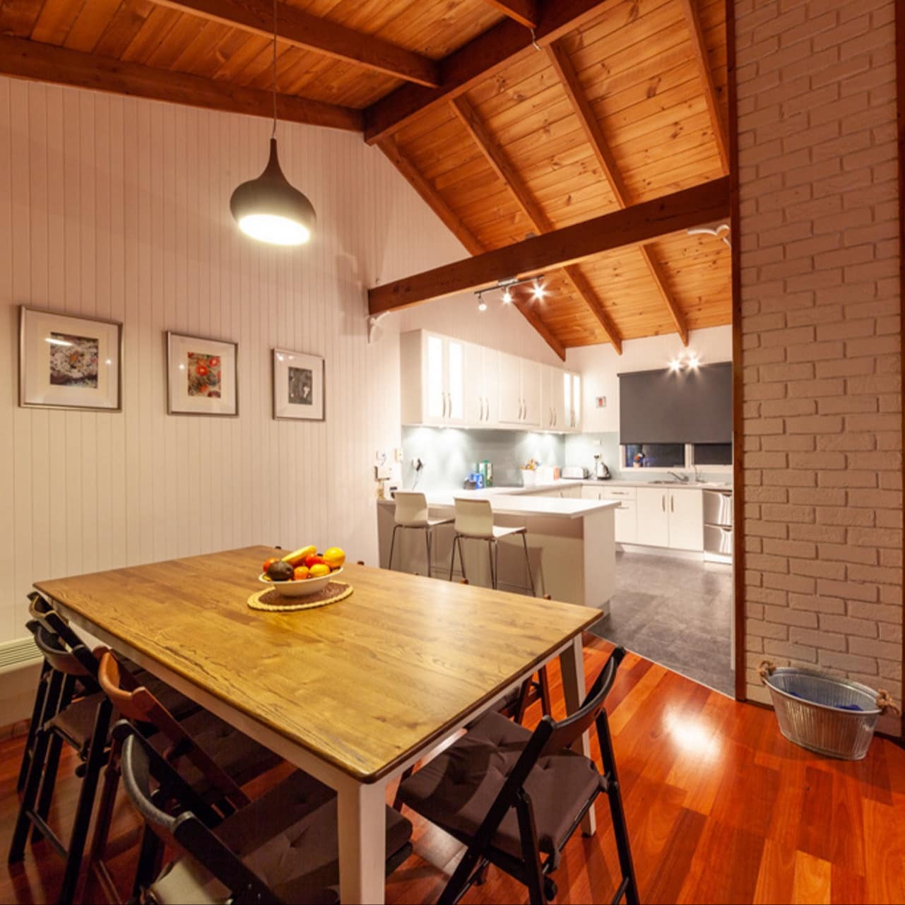 Open dining room and kitchen with hardwood floors, vaulted wood-panelled ceiling, wooden dining set, and sleek kitchen.