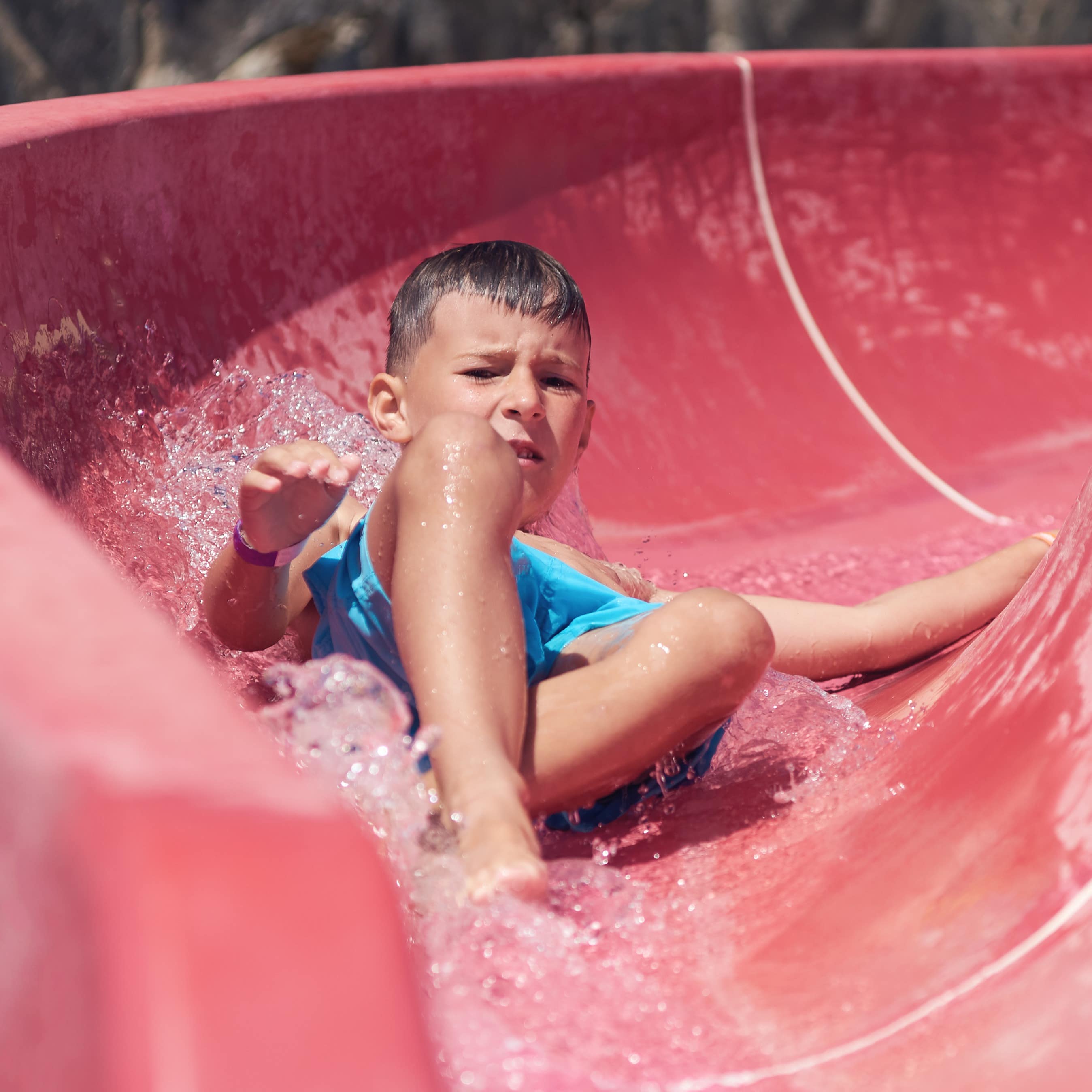 Little boy sliding down a red water slide