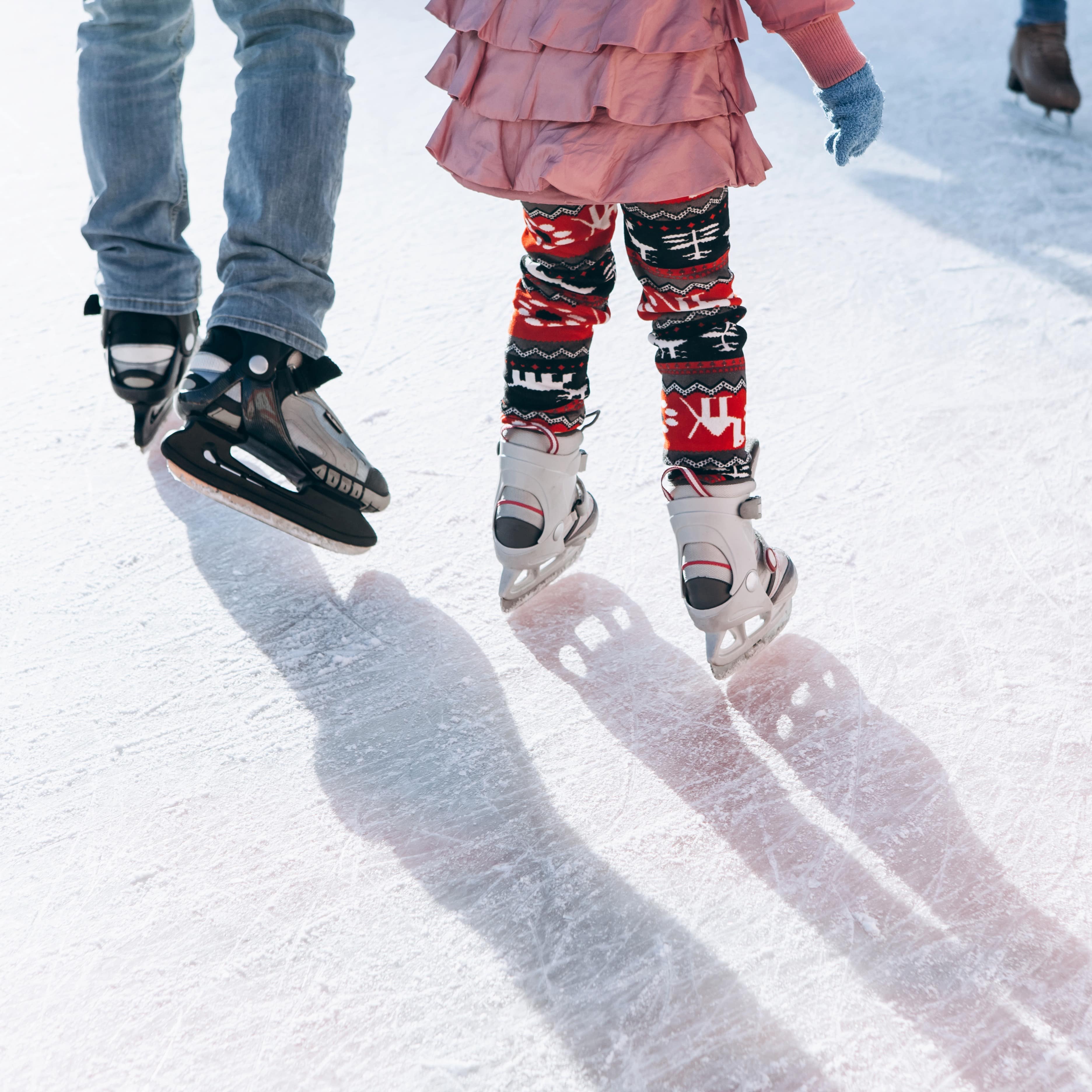 Legs and feet of a parent and child ice skating together 