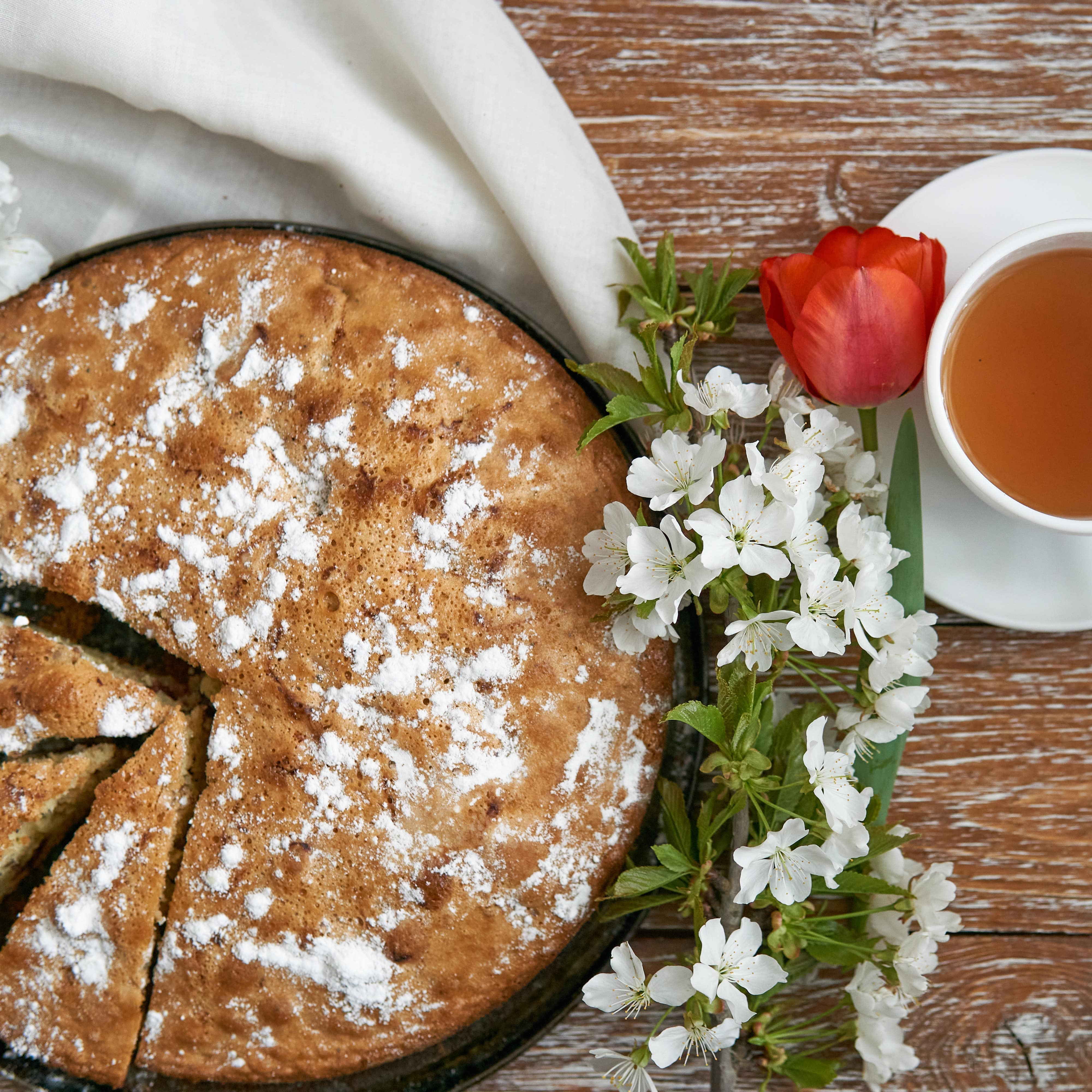 Apple pie sliced with apple blossom and flower and cup of tea on a wooden table