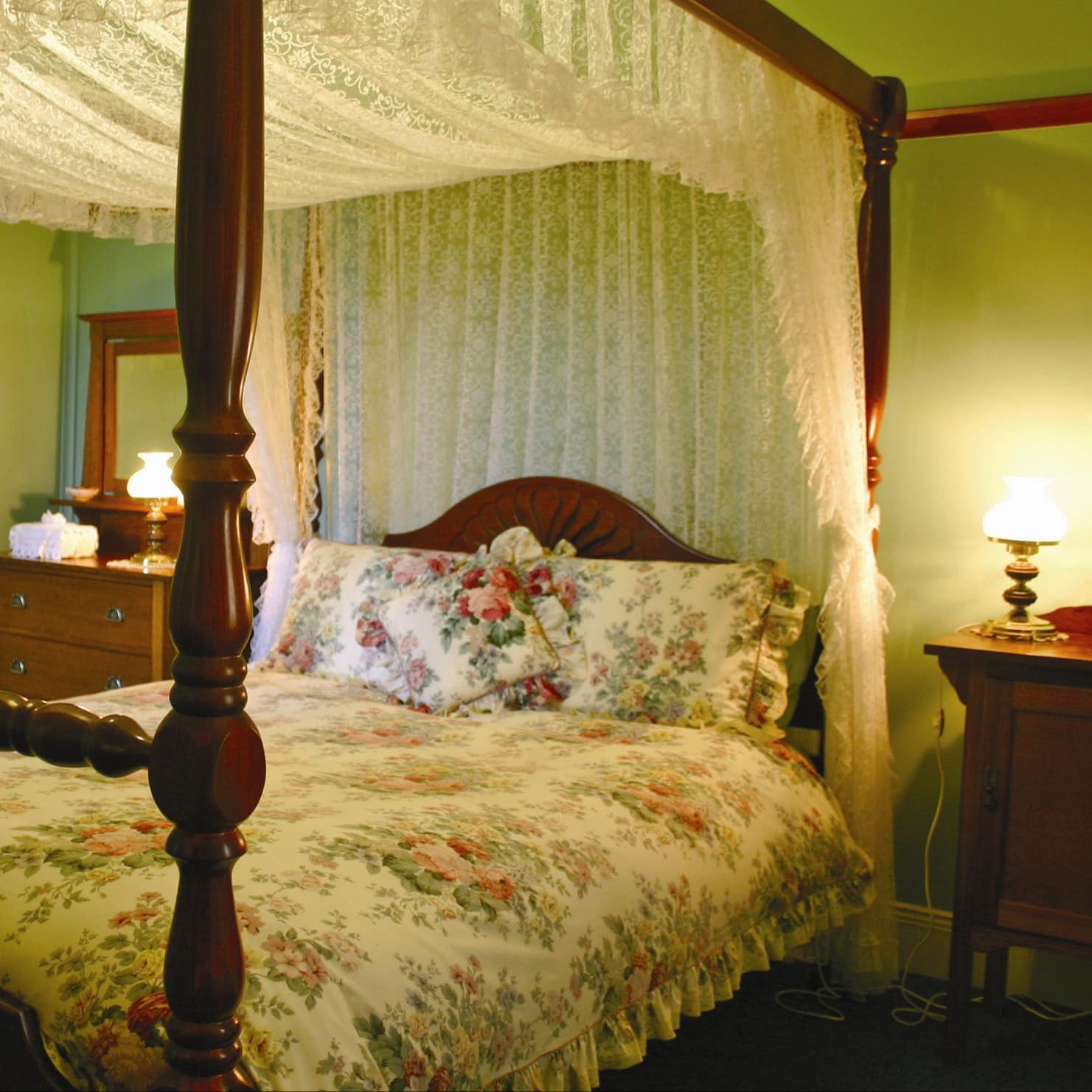 A vintage bedroom with green walls and a wooden canopy bed, floral bedding and lace canopy.