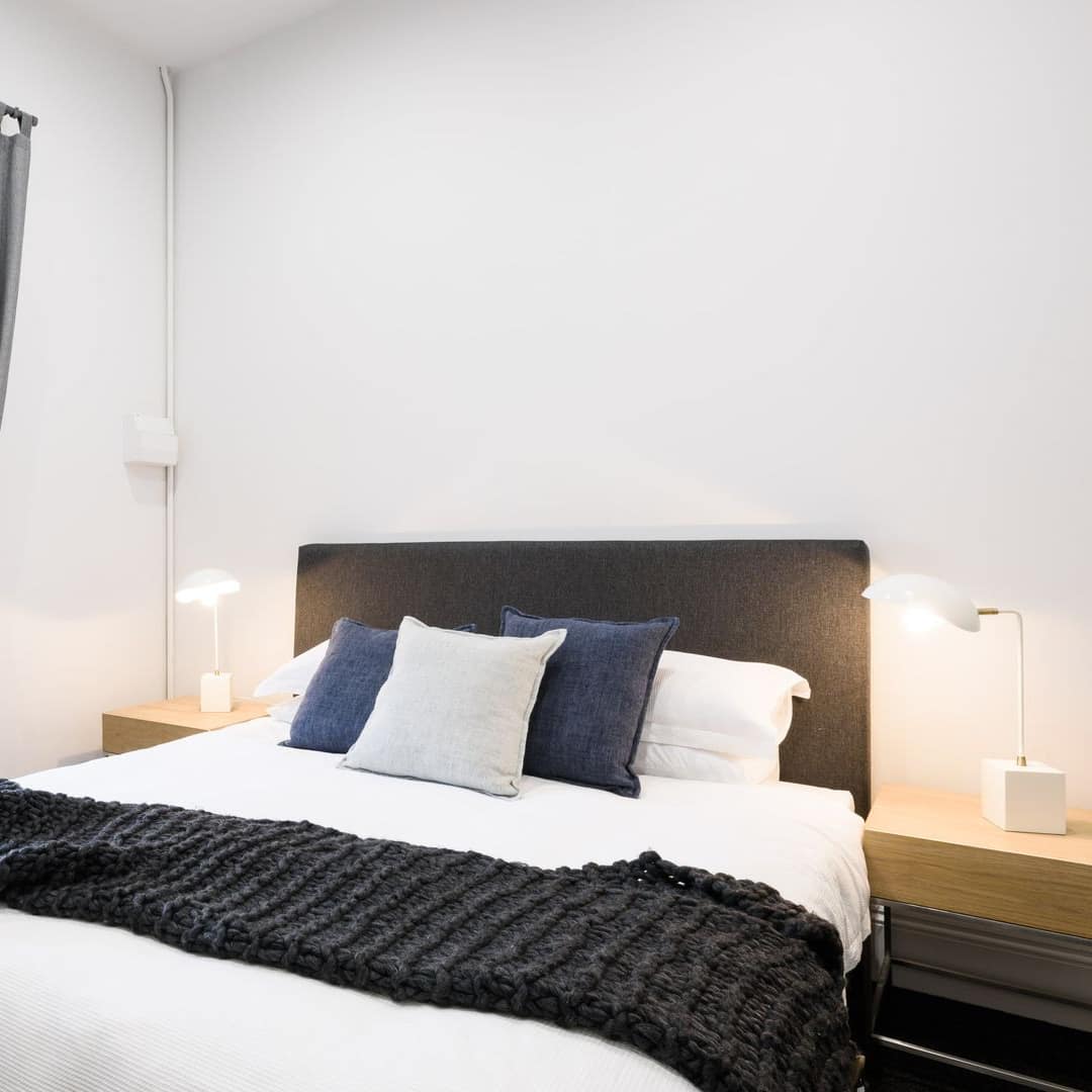 Bedroom with white walls, a king size bed, black and white bedding, and tall window with grey curtains.