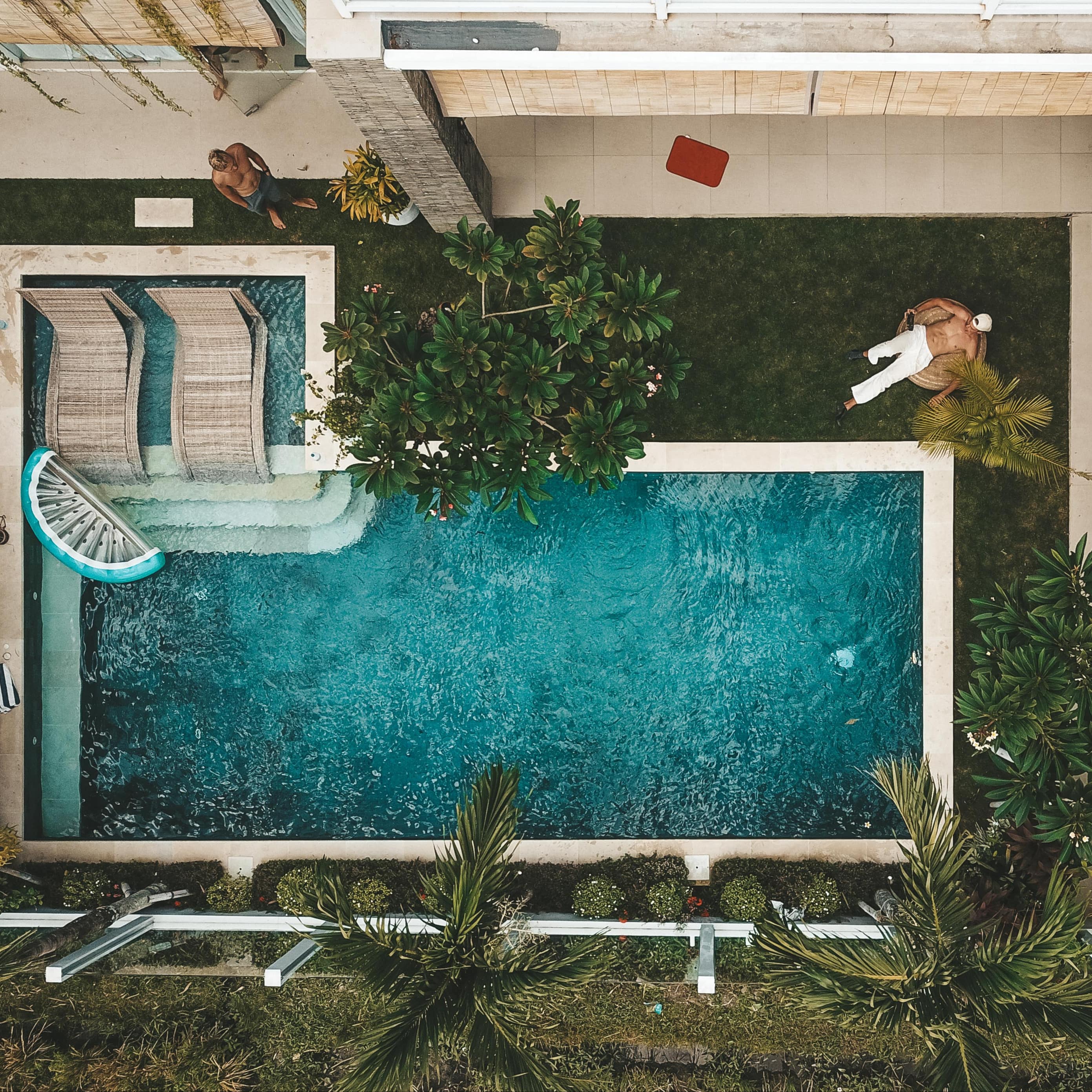 Aerial view of Bali villa with private pool and courtyard, lounges, a veranda with decorative vines and a man relaxing