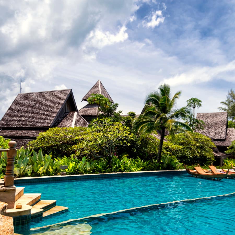 Large pool with floating lounges set against backdrop of Thai villas, tropical plants and palm trees