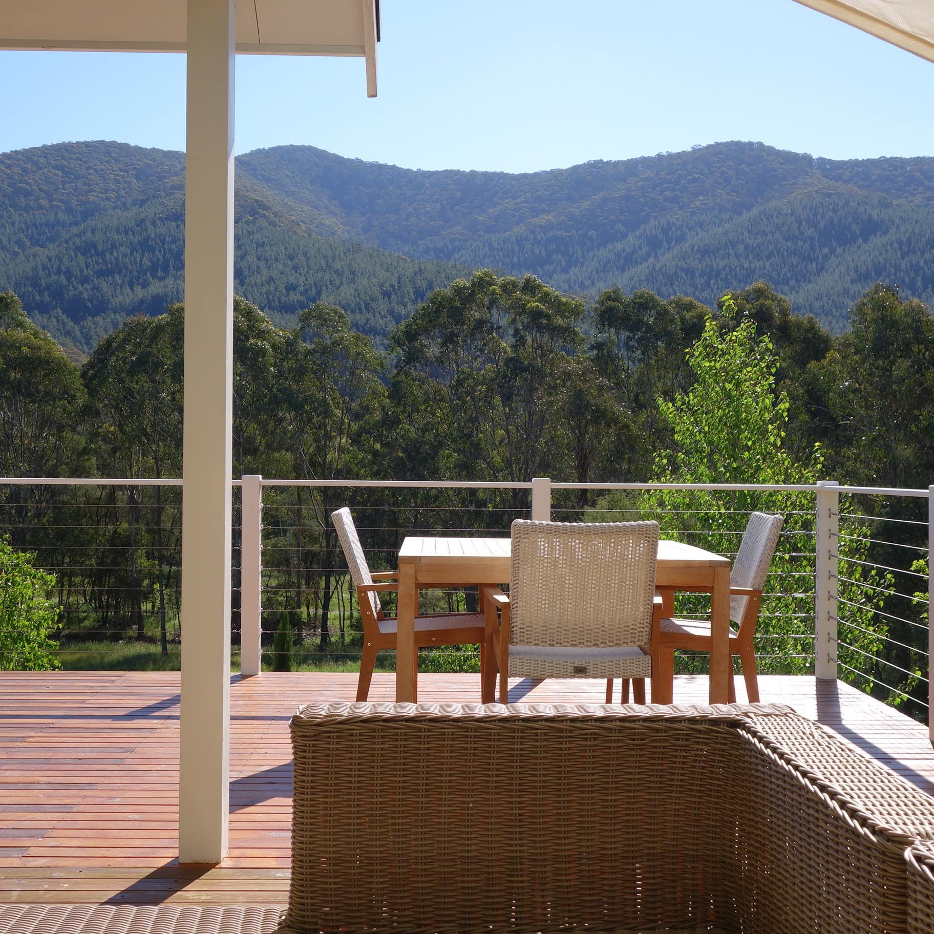 Wooden deck with metal railings, dining set, and wicker furniture overlooking mountainous landscape.