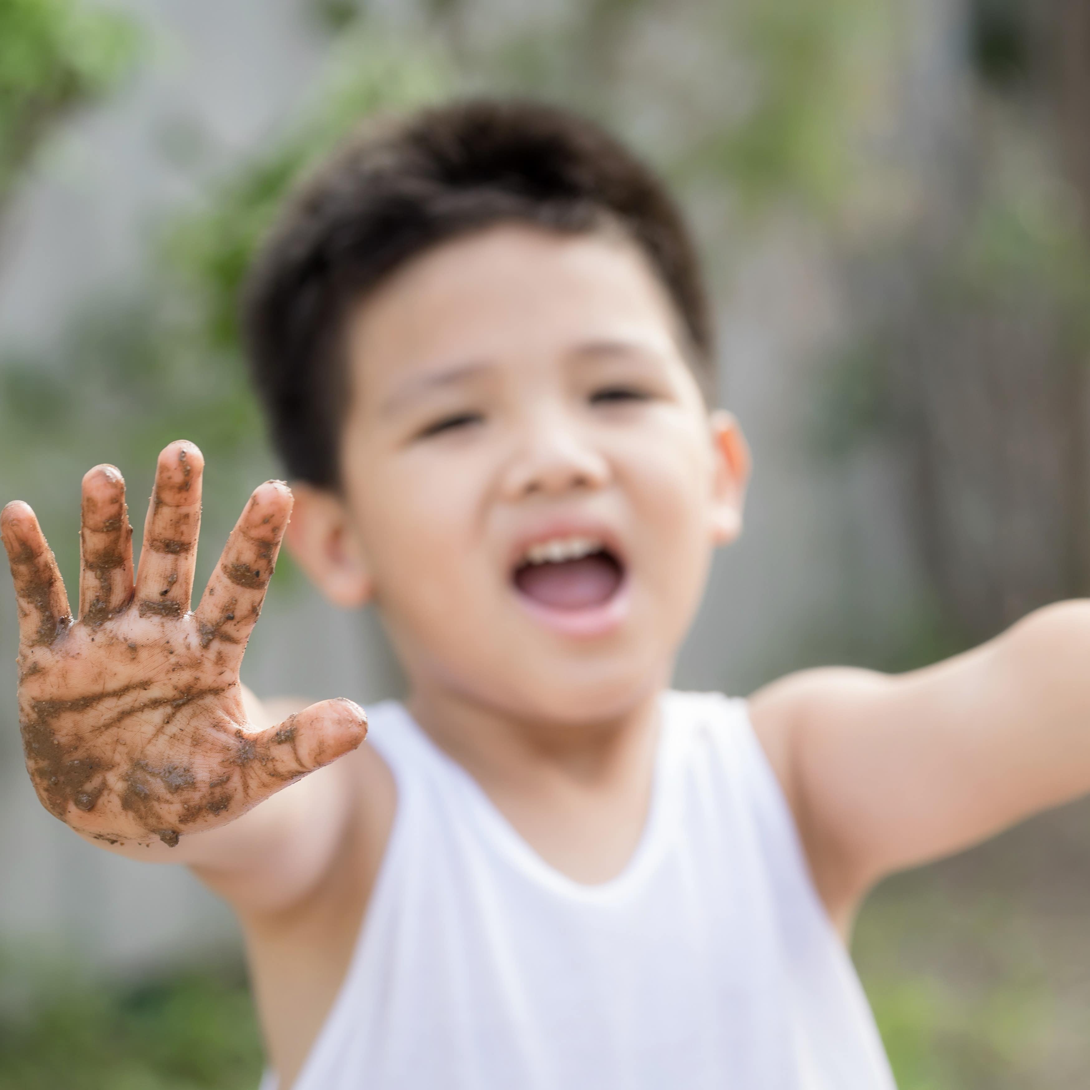 Smiling little boy holding muddy hands out while playing in the mud at park