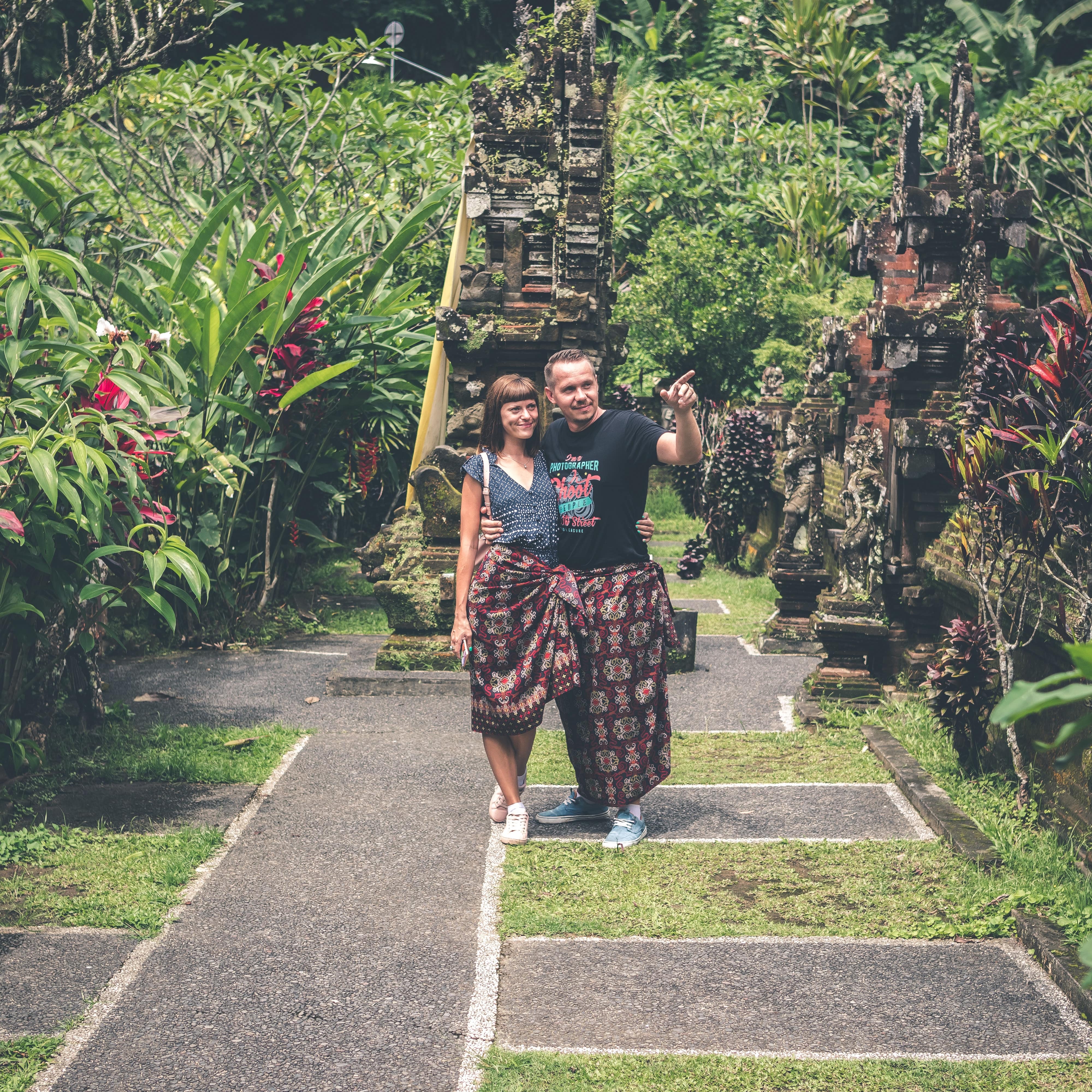 Couple in Balinese dress visit a temple garden with ornamental sculpture and vibrant fuschia and orange tropical plants