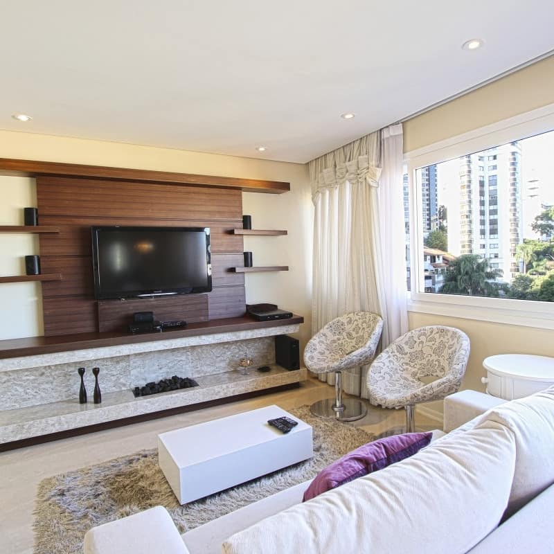 A modern apartment with a white, overstuffed couch, pod chairs, Scandinavian bookshelf with TV and windows with city views