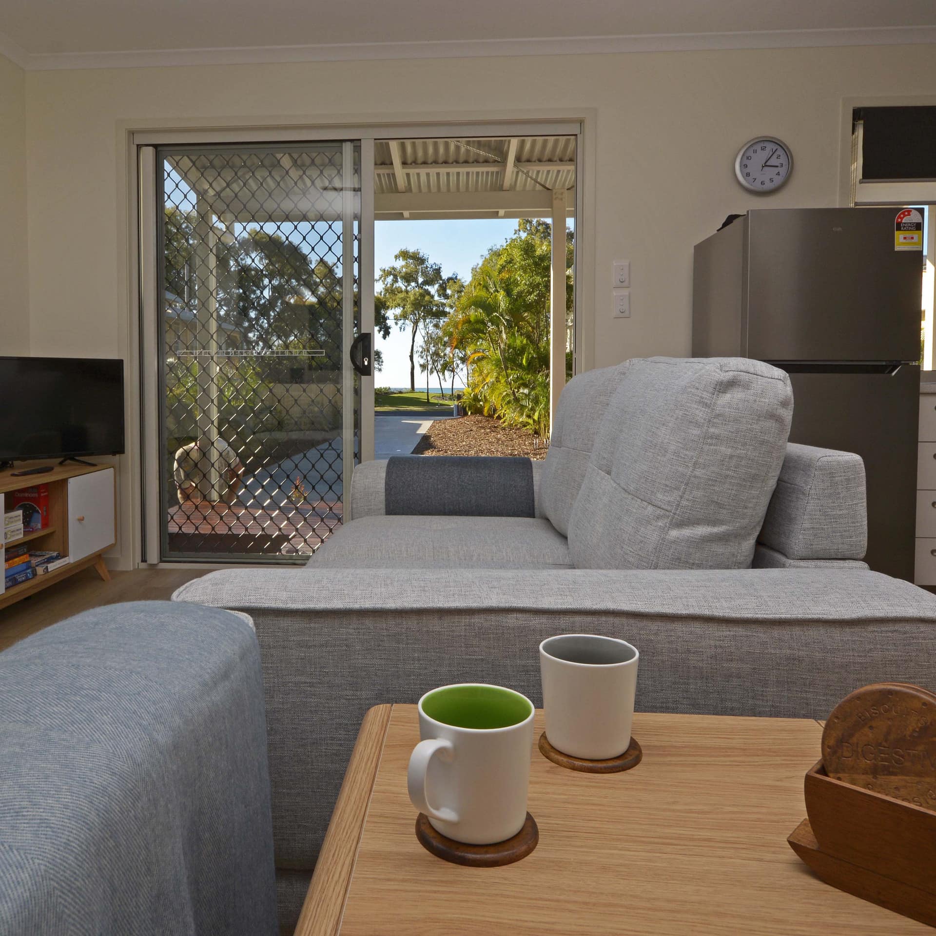 Interior of cottage with gray sofas, wood-look floors, stainless steel refrigerator, and sliding glass doors with bay view.