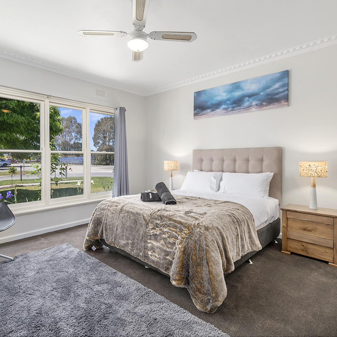 Spacious bedroom, grey carpet, shag rug, a king size bed, white bedding, fur blanket, wide windows with neighborhood views.