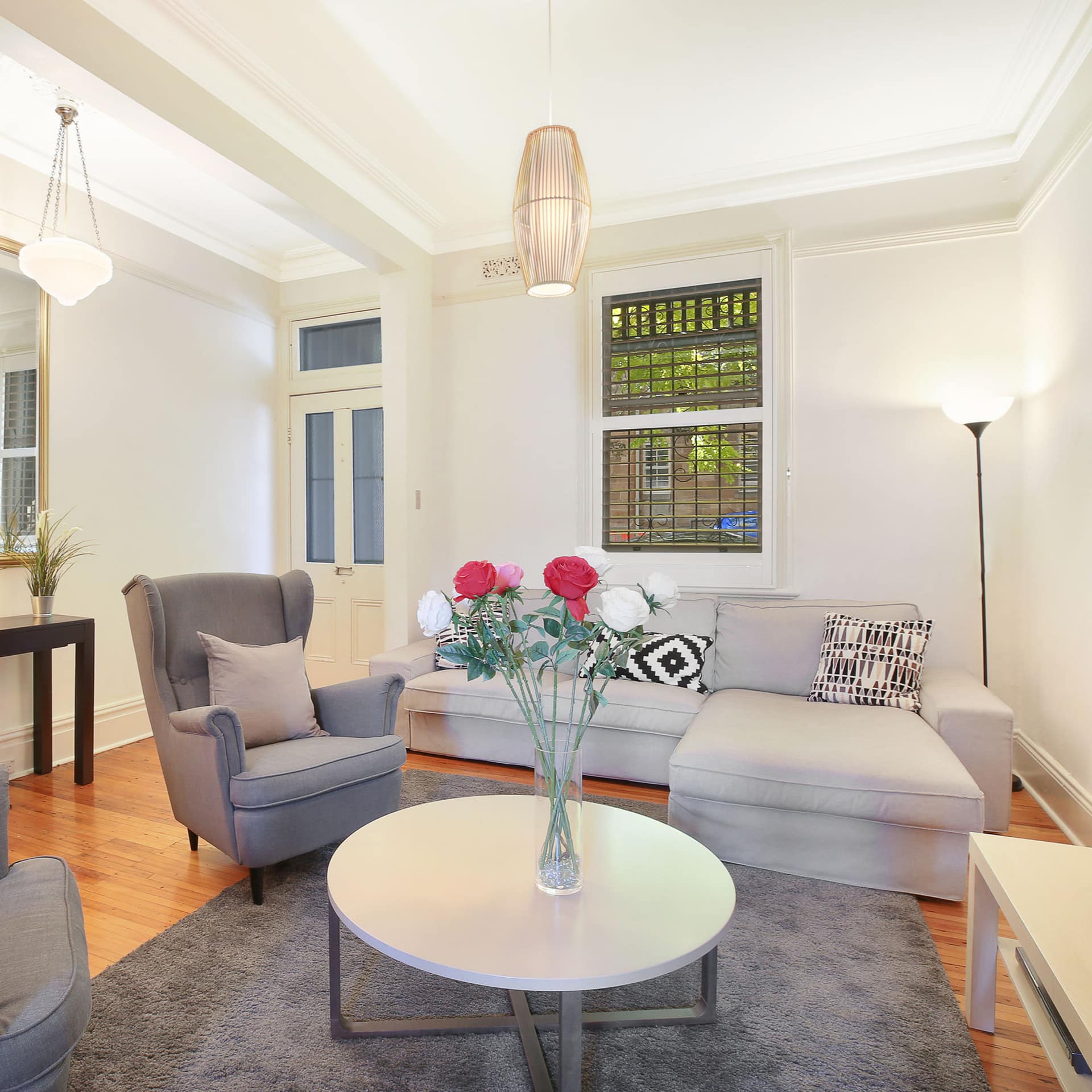 Bright living room with hardwood floors, white walls, grey chairs and sofa, round coffee table, and grey rug.