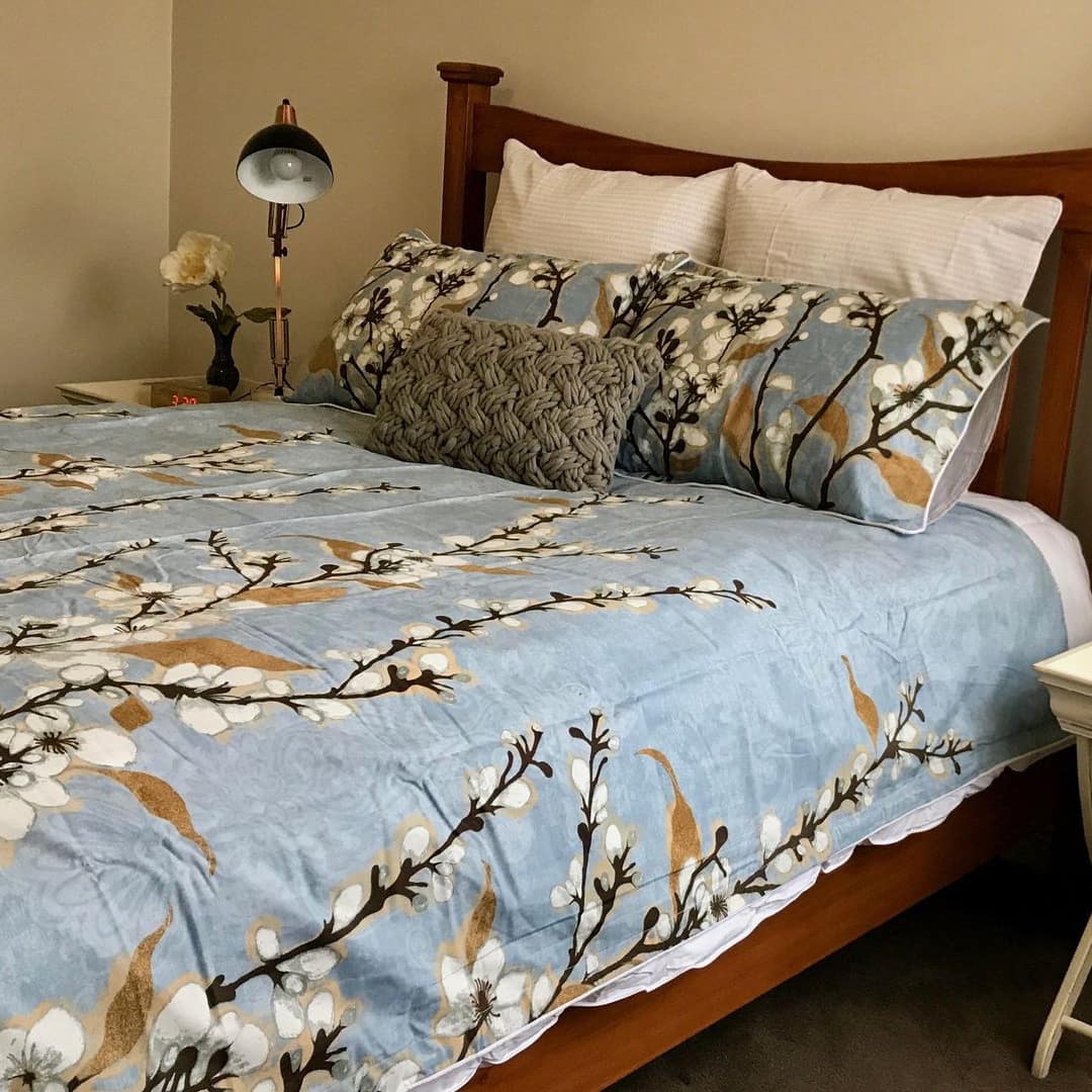 Bedroom with wood-framed queen size bed, blue floral bedding, matching white bedside tables with flowers and lamps.