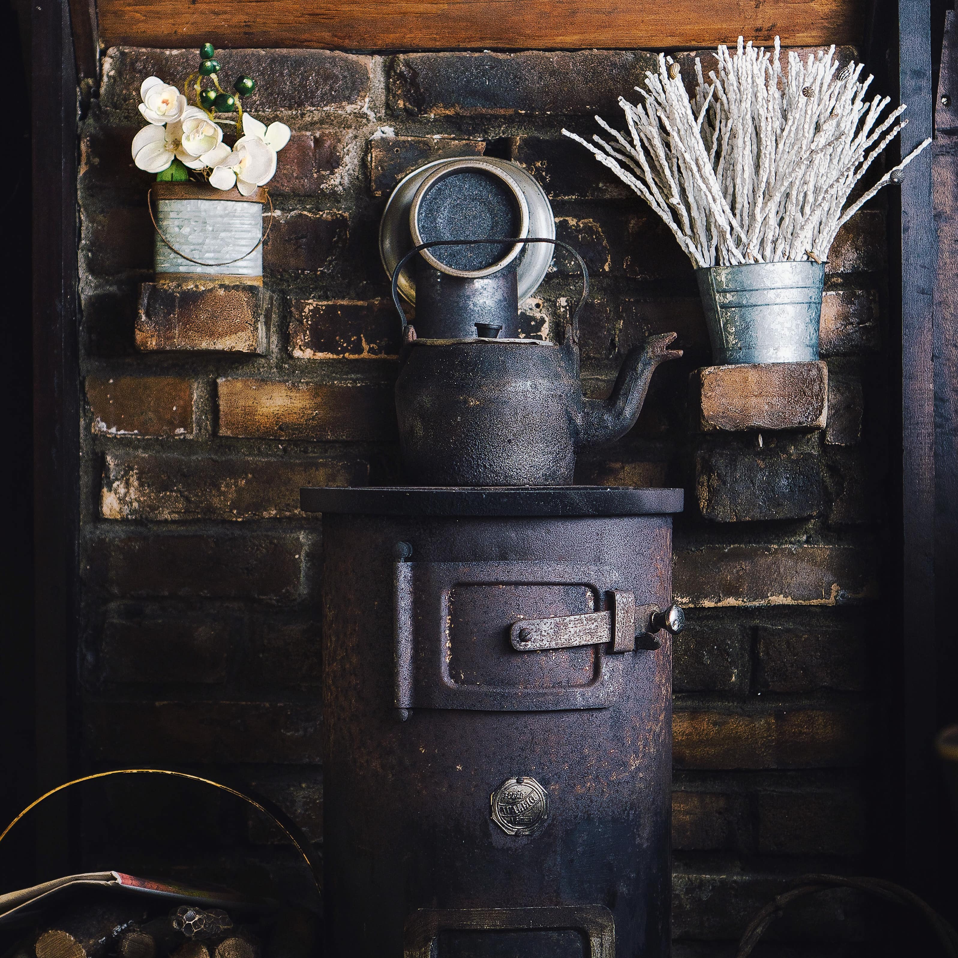 Antique metal stove against a brick background with a firewood basket and dried herbs