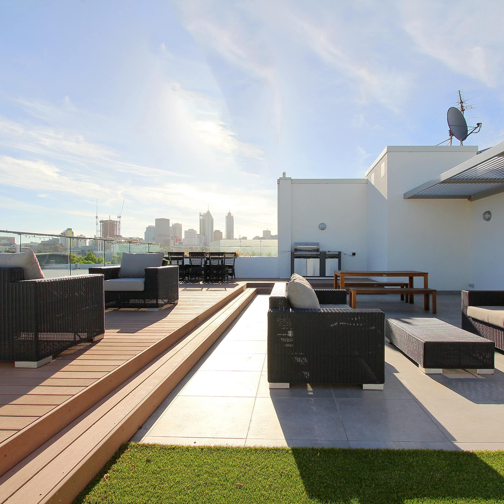 Sunny patio space with wicker outdoor furniture, black dining set, and glass railing, overlooking city views.