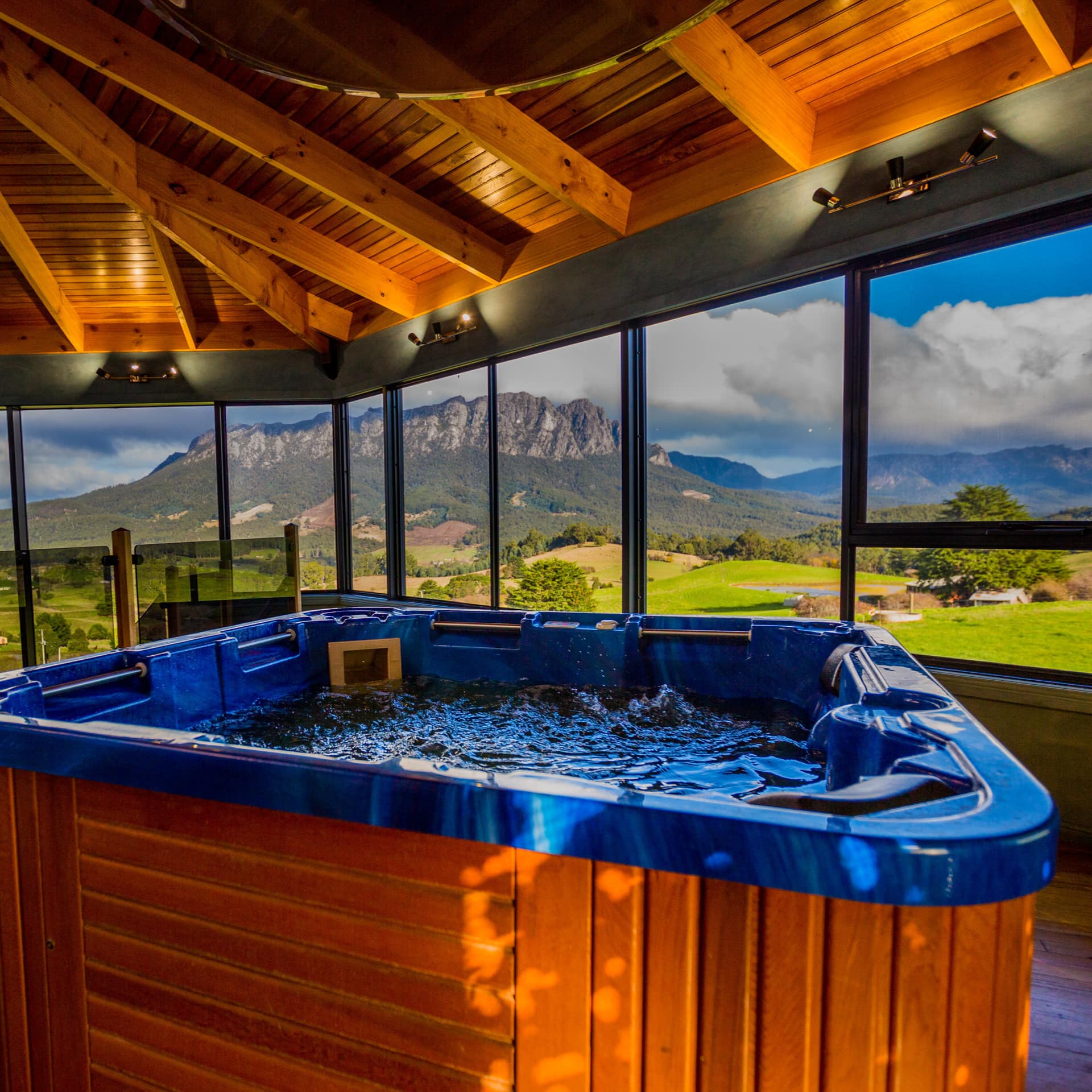Hot tub in 4-bedroom lodge with wooden ceilings and floors and a bank of windows looking out on Mt Roland and rolling hills