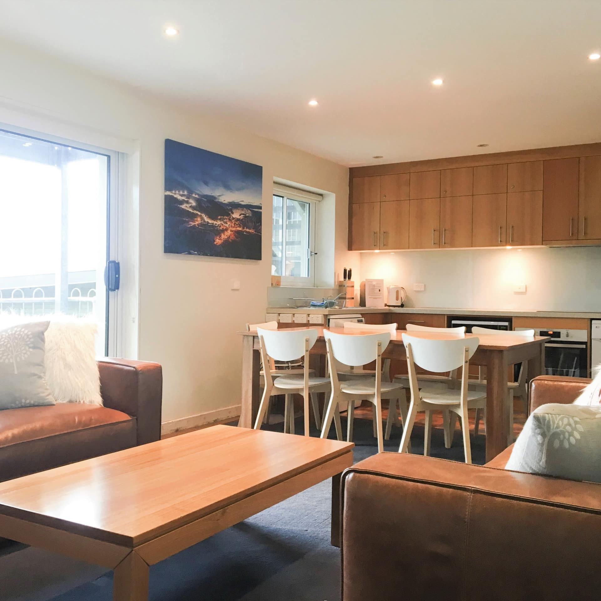 Modern living room and kitchen, brown leather sofas, wooden coffee table, wood kitchen cabinets and wooden dining set.