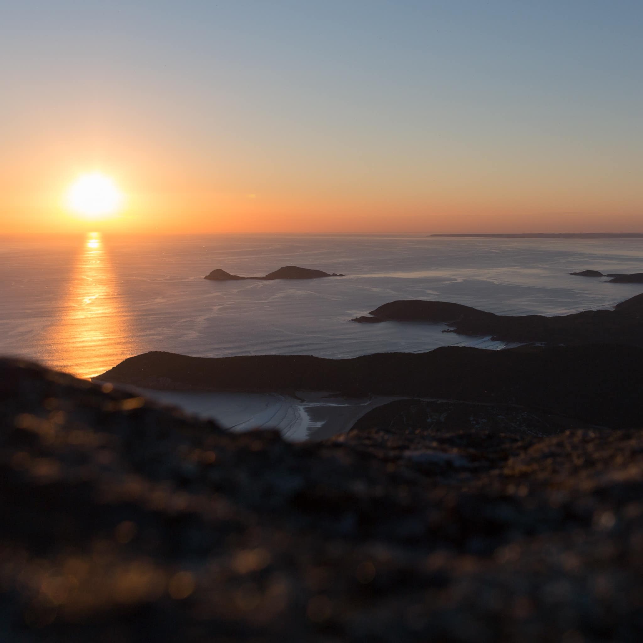 View from Mt Oberon in Wilsons Promontory at sunrise with light pink skies and sunlight reflecting off of rocks