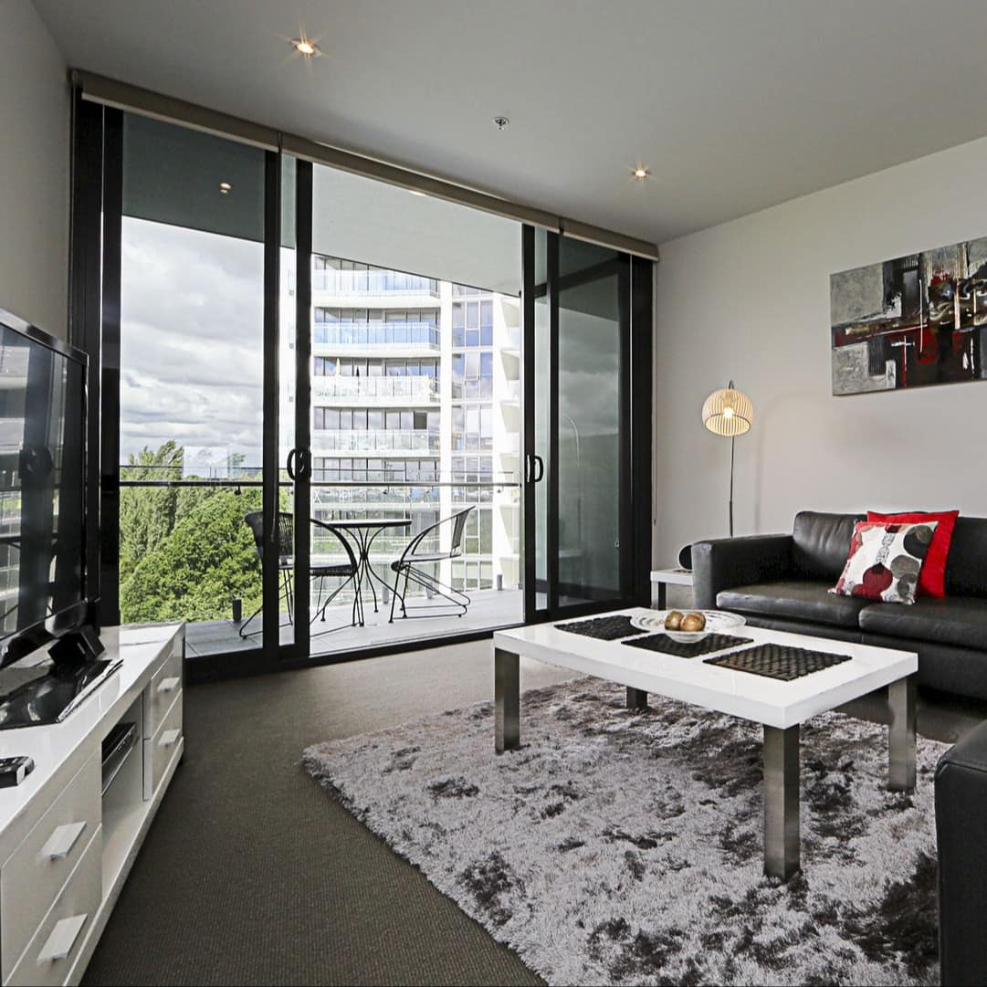 Living area of luxury apartment with grey leather sofa and chair, modern coffee table, TV and balcony with two-top table