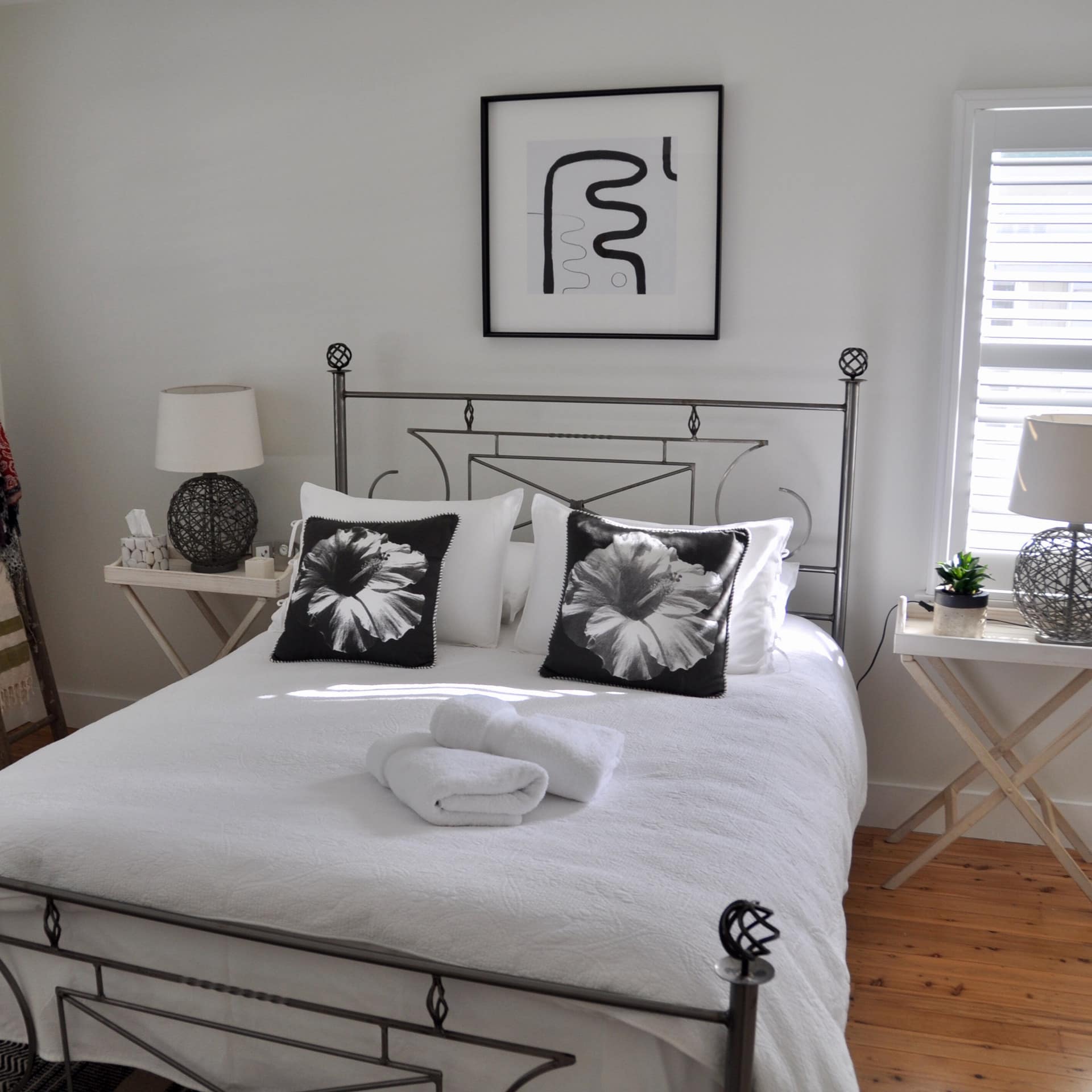 Bedroom in cottage with a queen size bed, white linen and black accents, and hardwood floors.