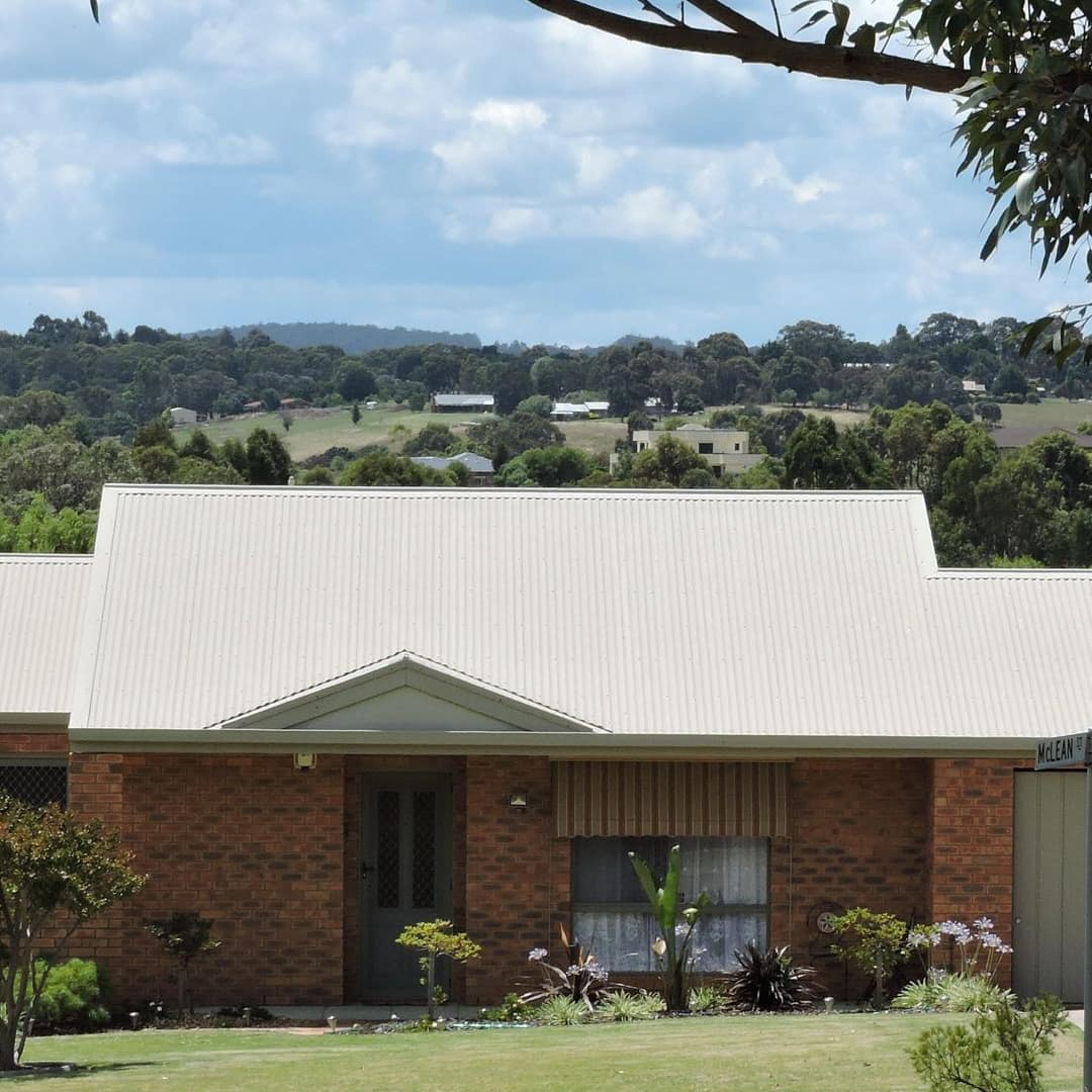 Brick cottage with a white roof, landscaped lawn, and rural countryside visible behind the home.