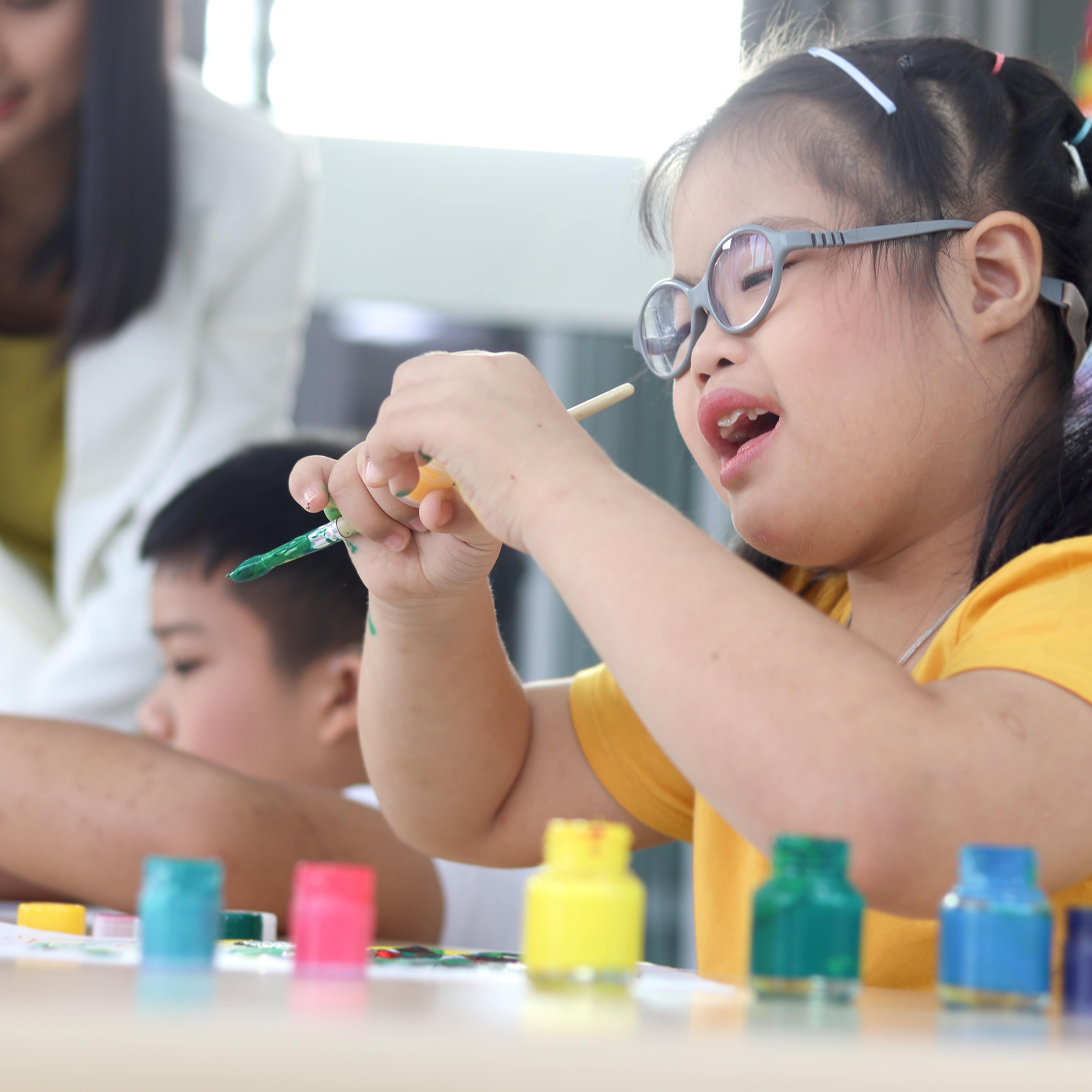 Young girl looks at paint on finger while holding paint brush in art class