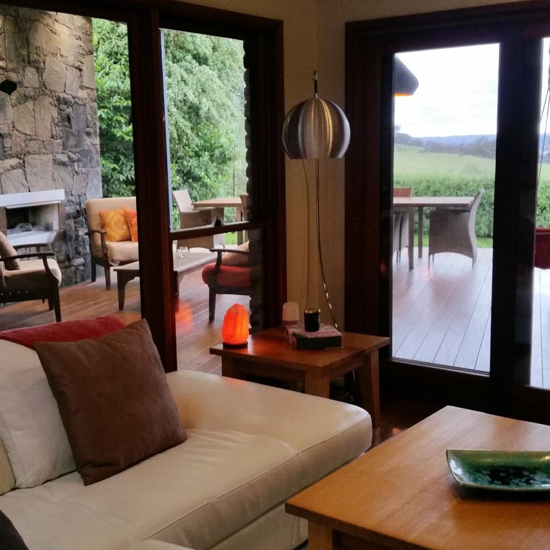 Cosy sitting area with large windows looking out at a patio with a built-in stone fireplace and view of the green landscape