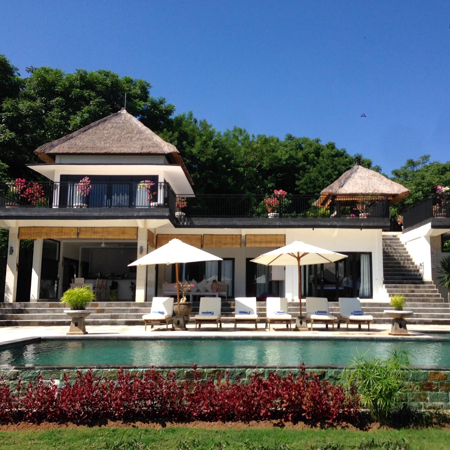 View of a two-story home with a balcony and ground-floor patio space and a pool with white lounge chairs.