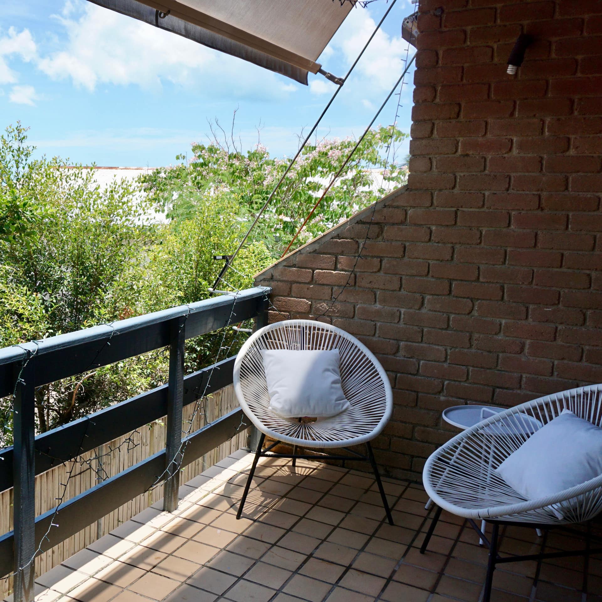 Covered balcony with tan tile floor and black railings, white woven round chairs, ocean views.