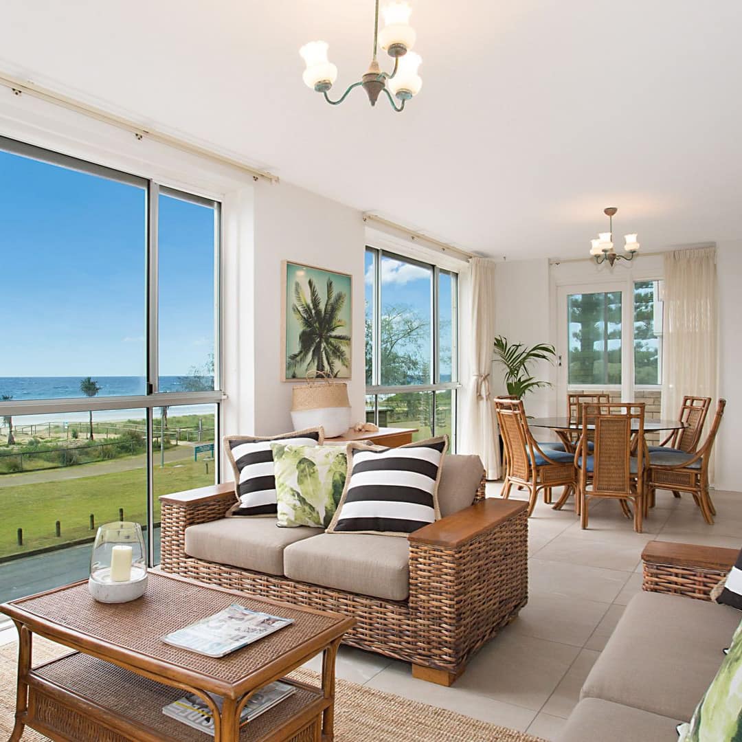 Open living and dining area of beachside apartment with cushioned wicker sofas, table and dining table and ocean view