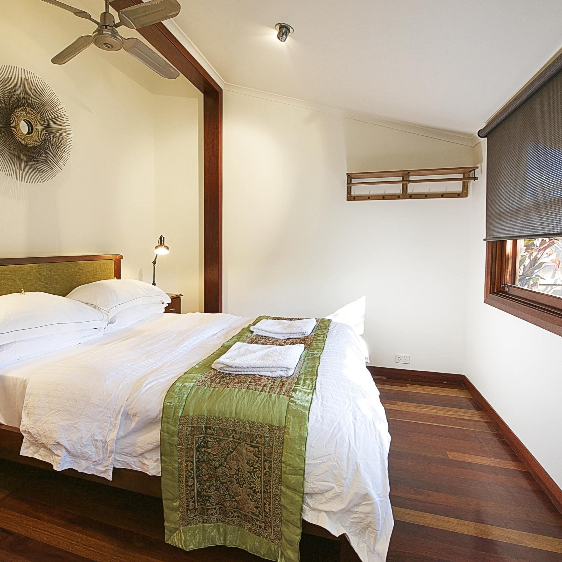Bedroom with hardwood floors, white walls, a king size bed, white and green bedding, and wide windows.