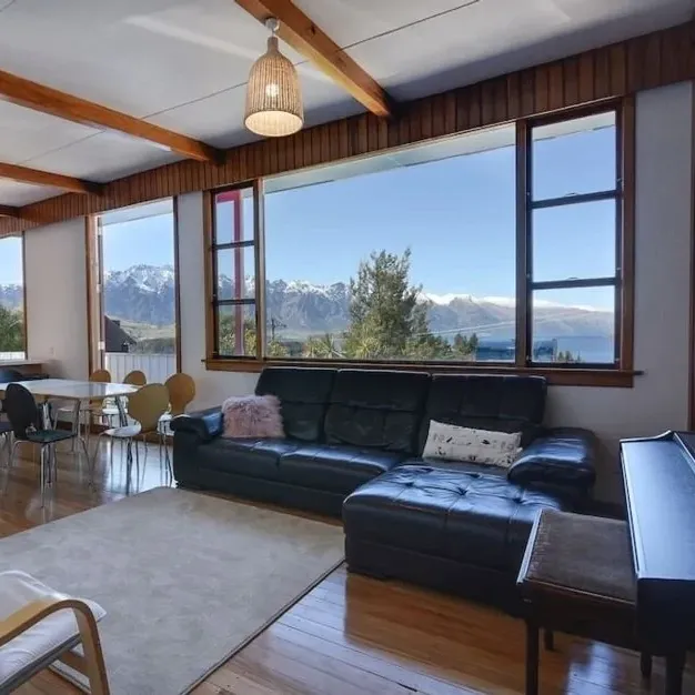 The living room of a family holiday home with couches and a piano with a view of mountains through the windows
