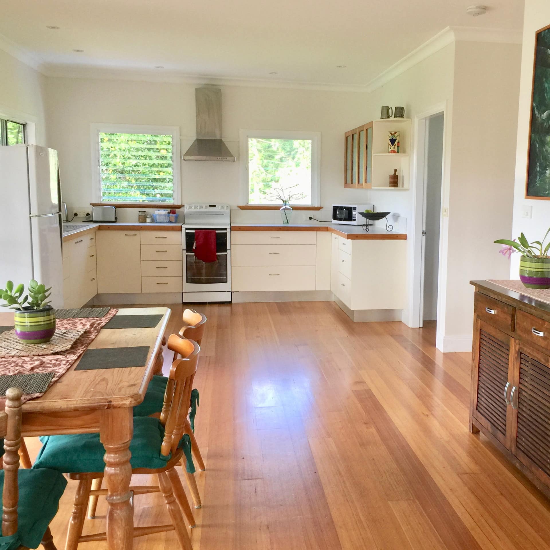 Open dining room and kitchen, hardwood floors, wood dining room set, and white, modern kitchen cabinets.