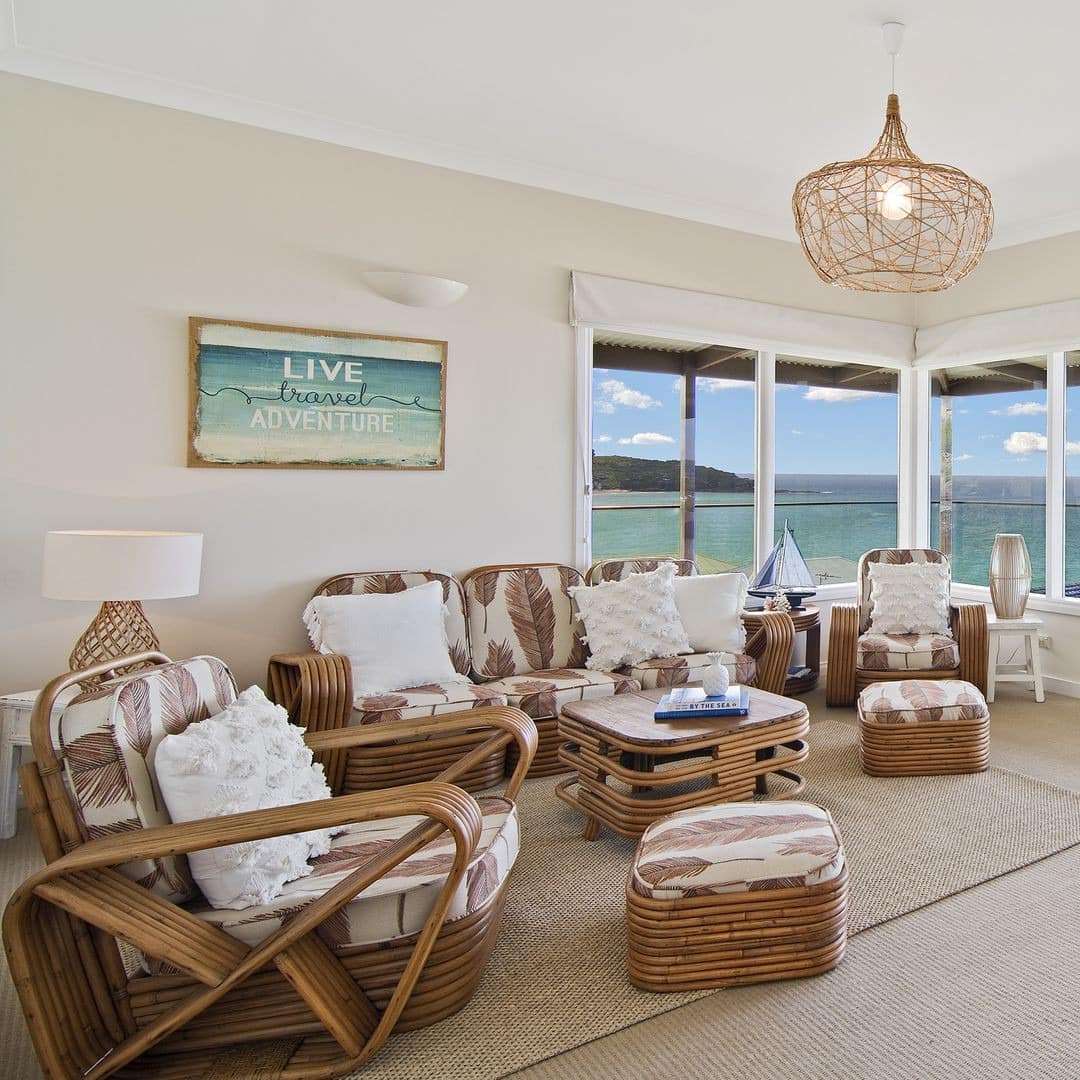 Open living room furnished in beige and brown, panoramic views of the ocean, bamboo wood furniture, basket weave lighting.