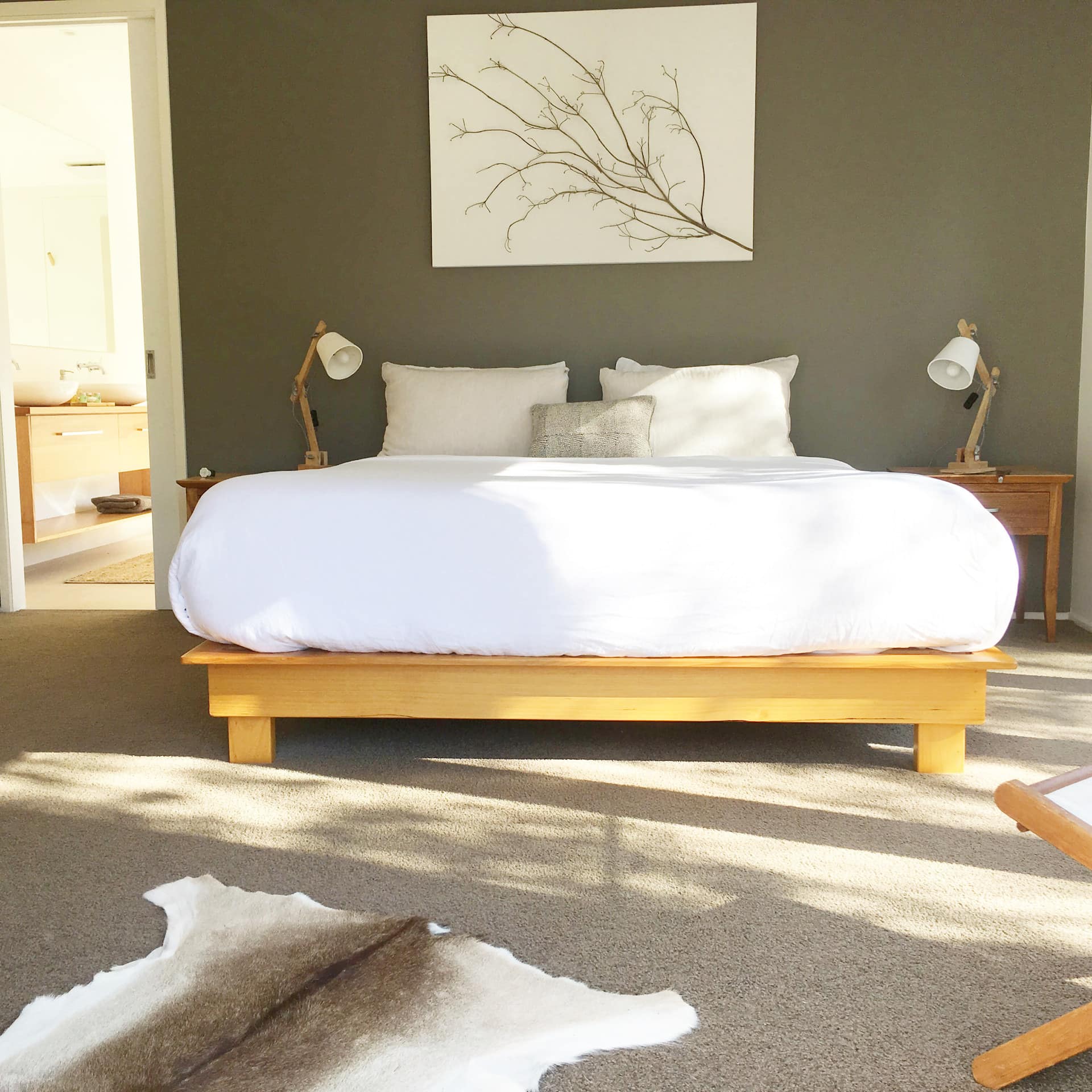 Sunny bedroom with grey carpet, green walls, a king size bed, white bedding, and fur rug.
