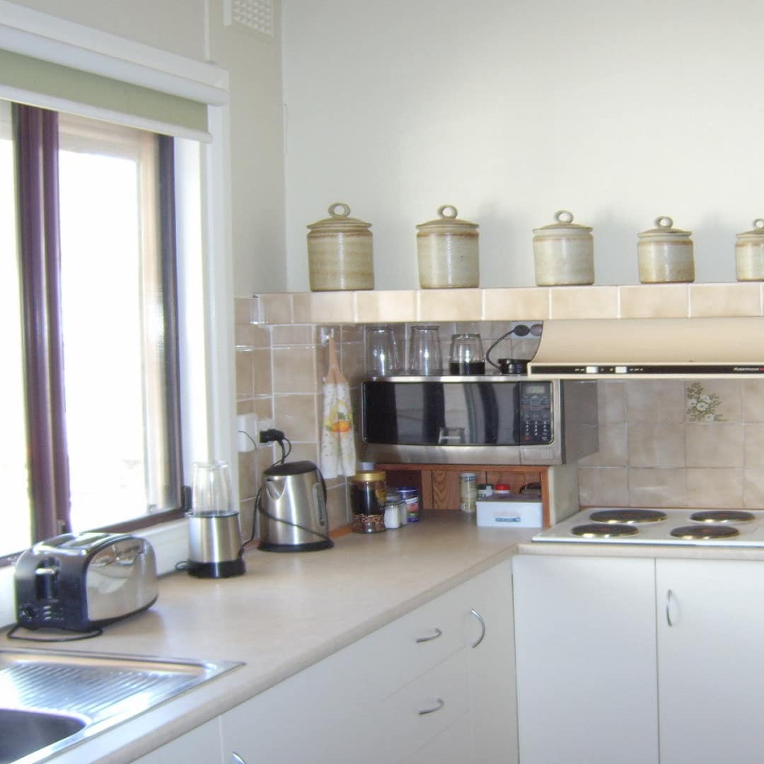 Kitchen with beige countertops and backsplash, white cabinets, glass shelves and appliances on countertops.