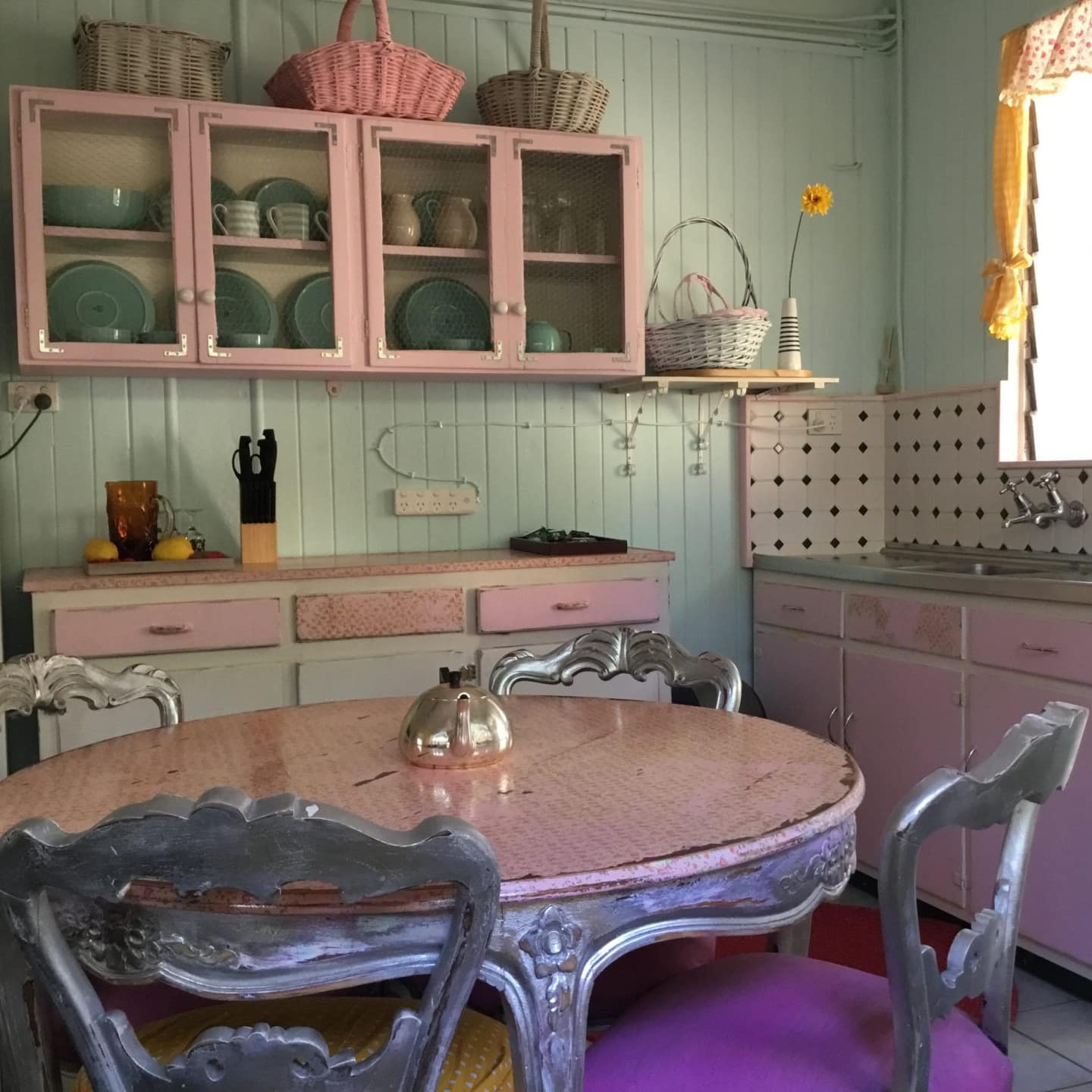 Charming, vintage kitchen with mint green walls, pink cabinets, pink round dining table, black and white tile backsplash