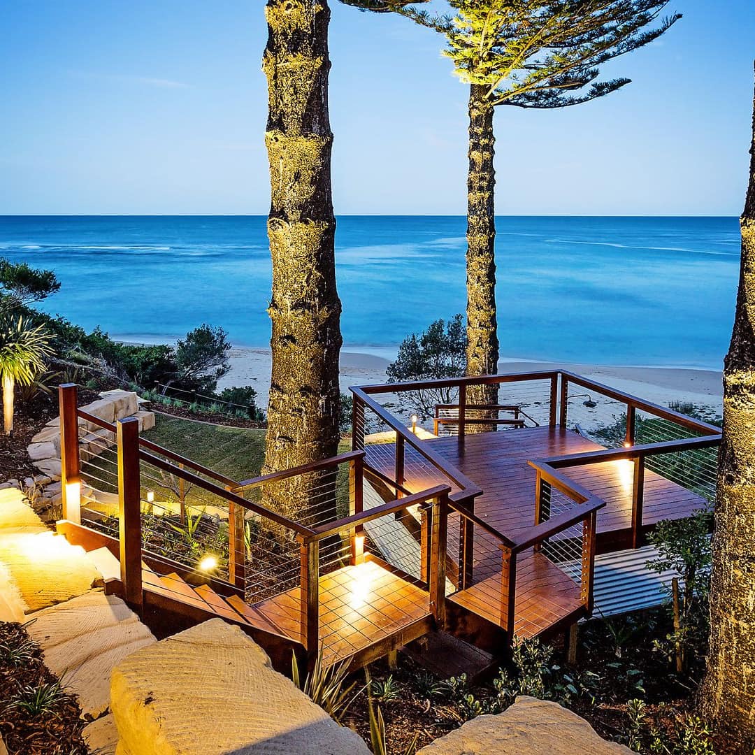 Detached hardwood deck overlooking the ocean, surrounded by palm trees, natural stone path.