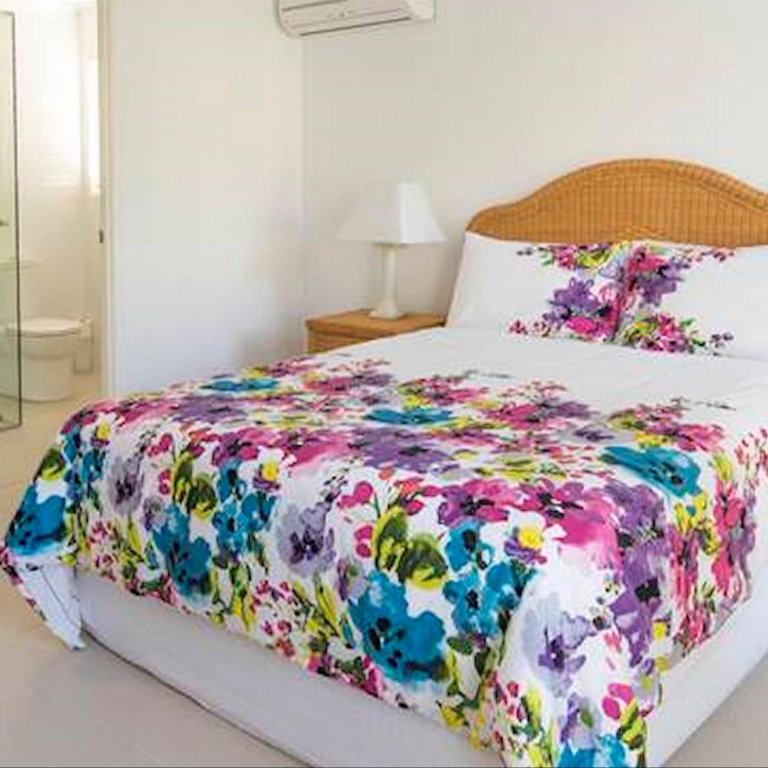 Bedroom with beige carpet and white walls, matching brown wicker bed and bedside tables, queen size bed.