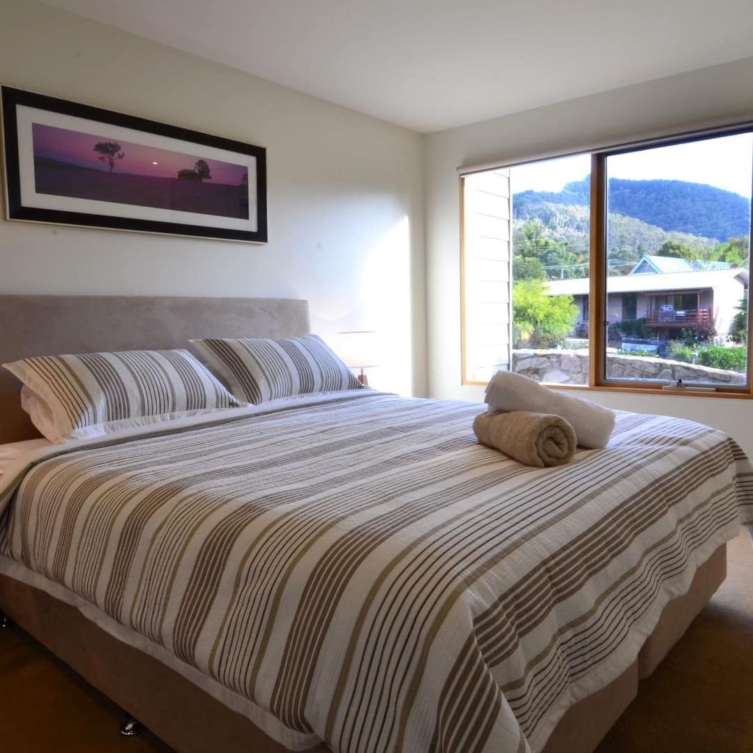 Bedroom with tan carpet, king size bed, tan and white bedding, rolled towels on bed, window with mountain views.