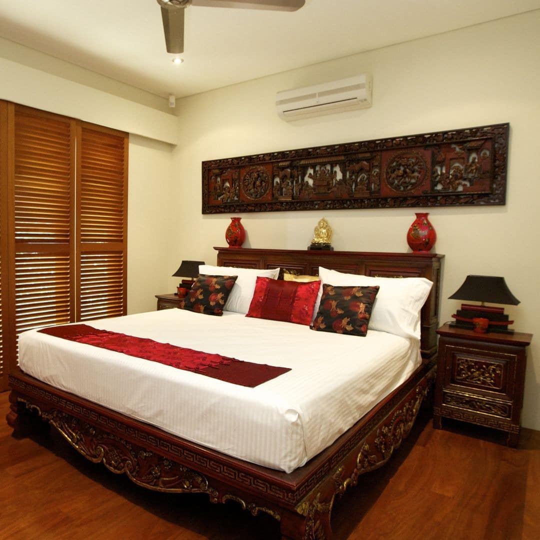 A bedroom with East Asian-inspired decor, hardwood floors, a king size bed with wooden ornately engraved bed frame.