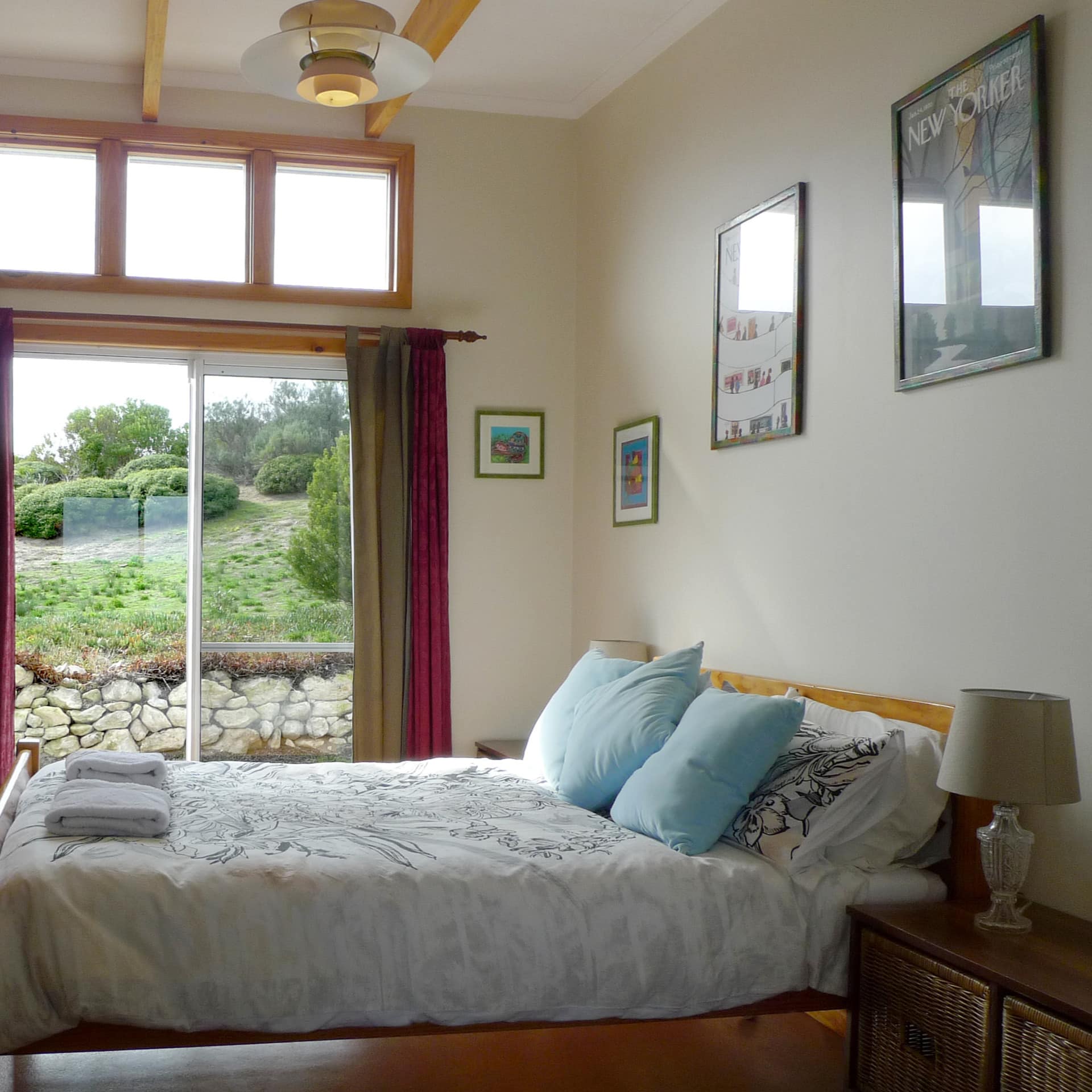 Bedroom with hardwood floors, a wood-framed king size bed, white and blue bedding, sliding glass doors with nature views.