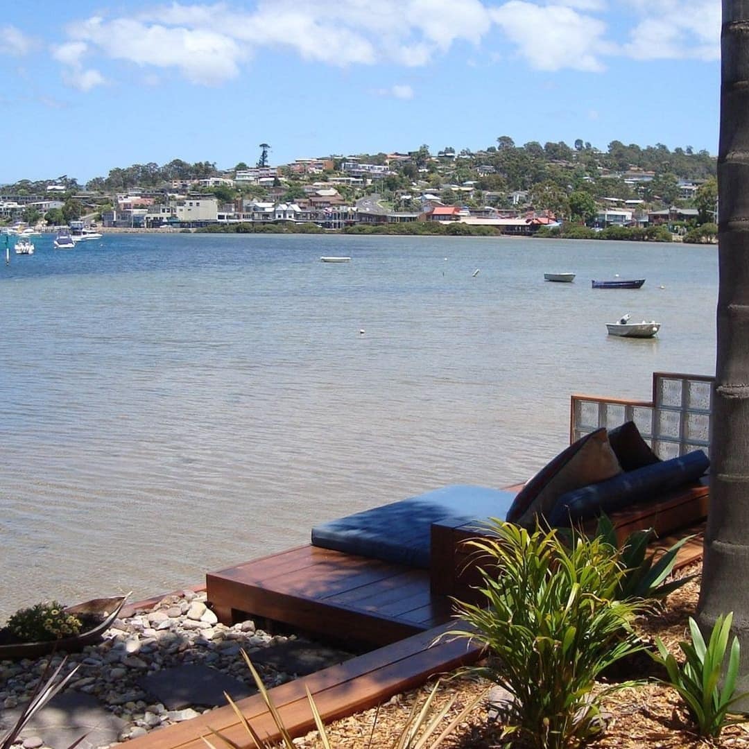 Wooden bench set in a landscaped garden with tropical plants overlooking Merimbula Lake.