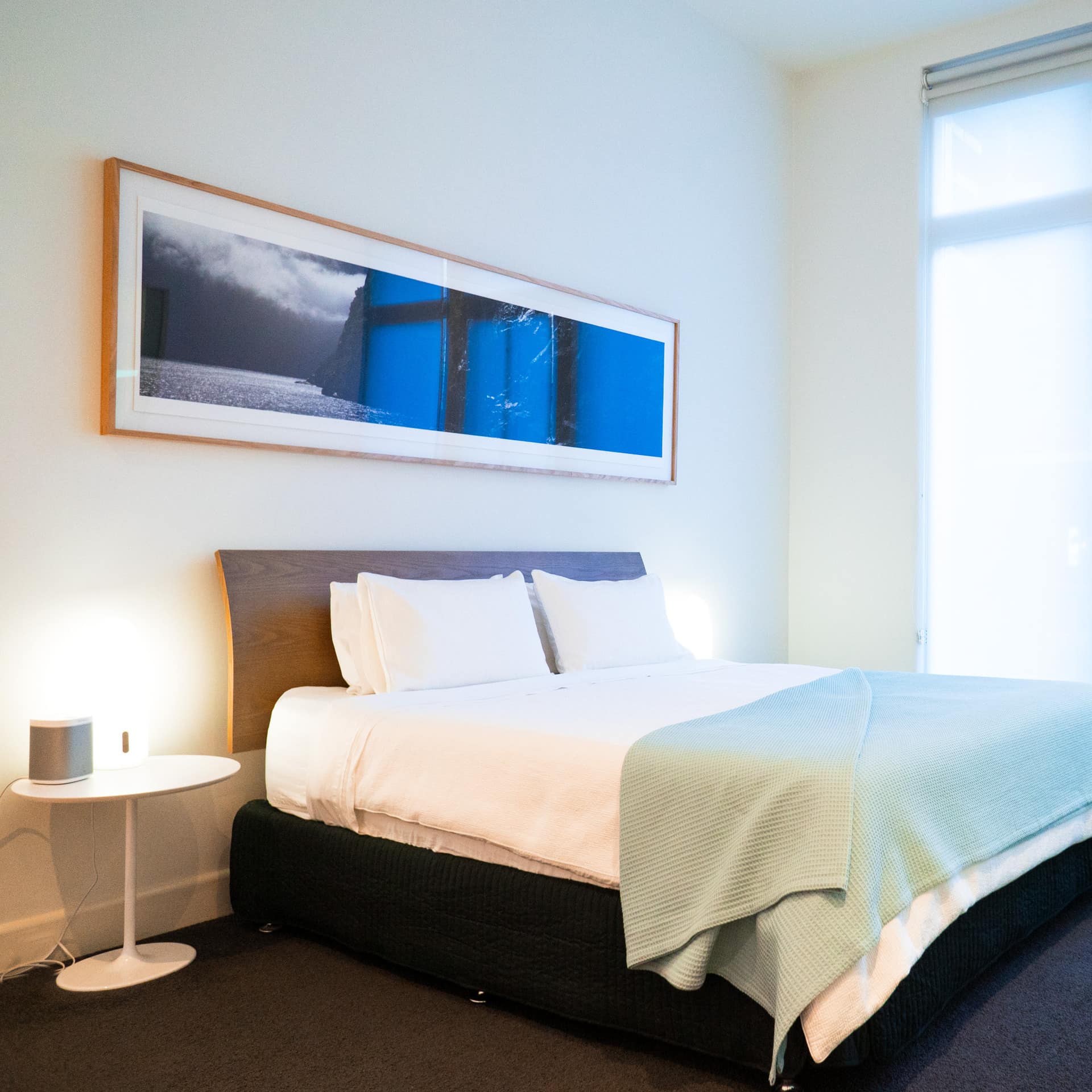 Spacious bedroom with grey carpet, white walls, a king size bed, white and green bedding, and tall windows.