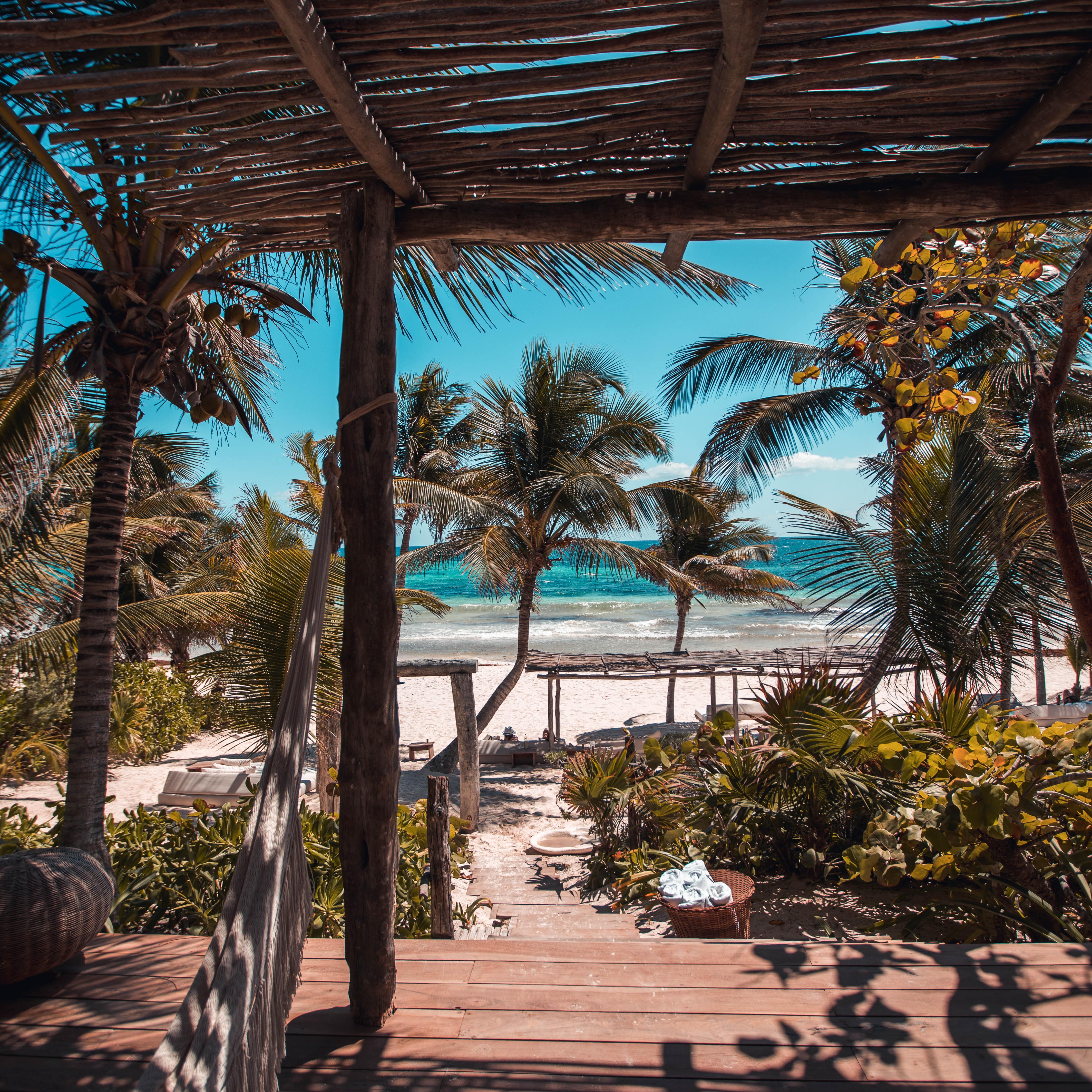 Wooden deck of villa with hammock, tropical garden and palms at the beach with azure water
