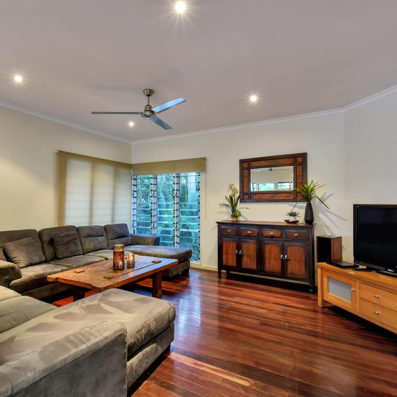 Open living room with hardwood floors, white walls, grey suede sectionals, flat-screen TV, natural wood coffee table.