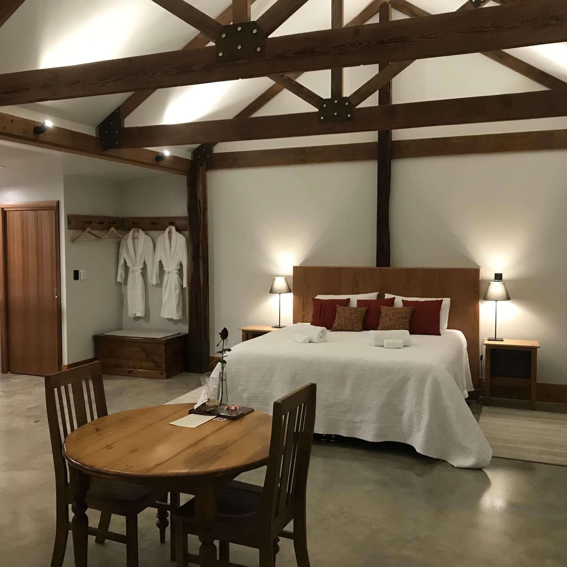 Spacious studio space, grey stone floor, vaulted ceiling with exposed beams, King size bed, and wooden dining set.